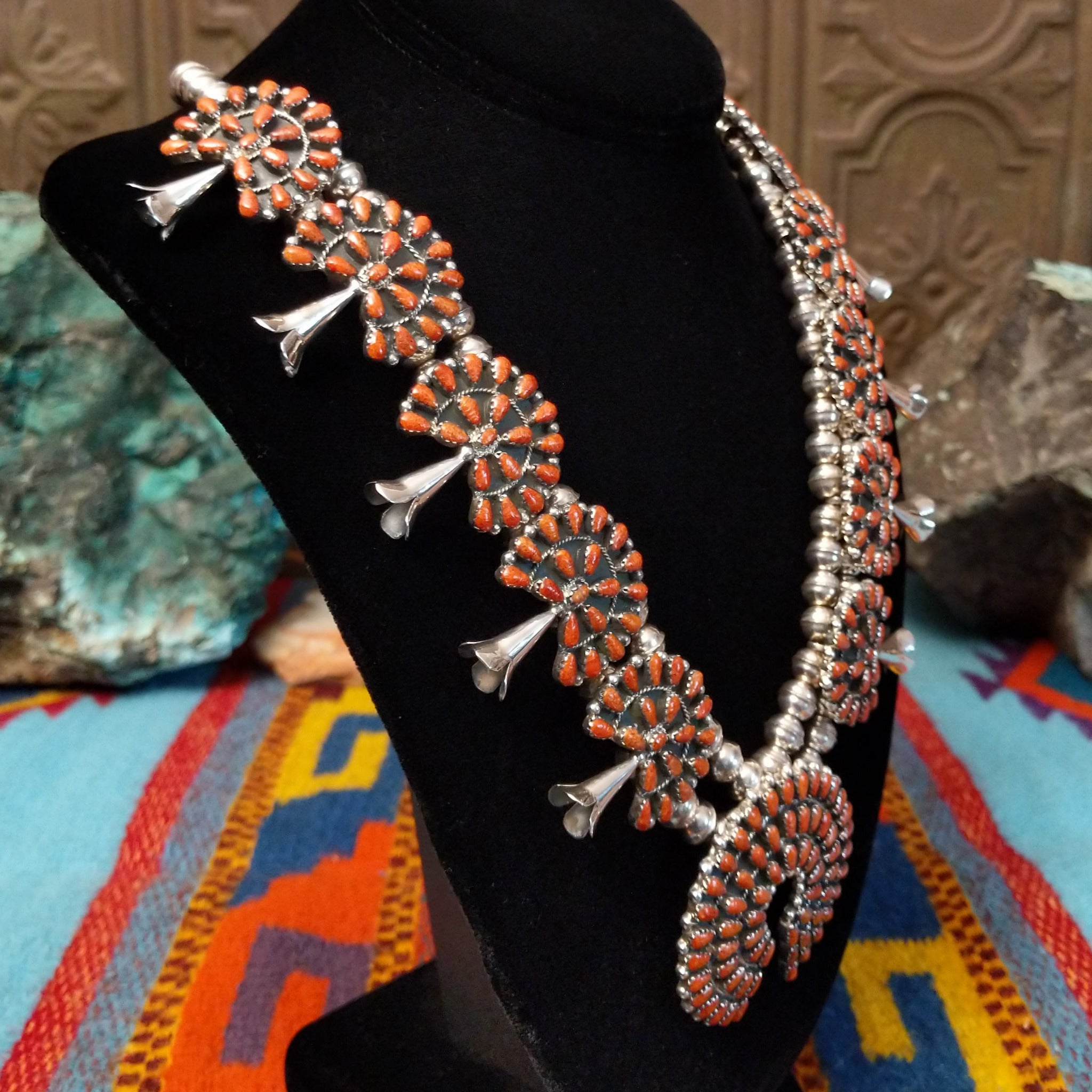 Navajo sterling silver squash blossom necklace and matching earrings by B.Y., featuring numerous red-orange coral stones arranged in floral clusters and a large coral-covered Naja pendant; side view.