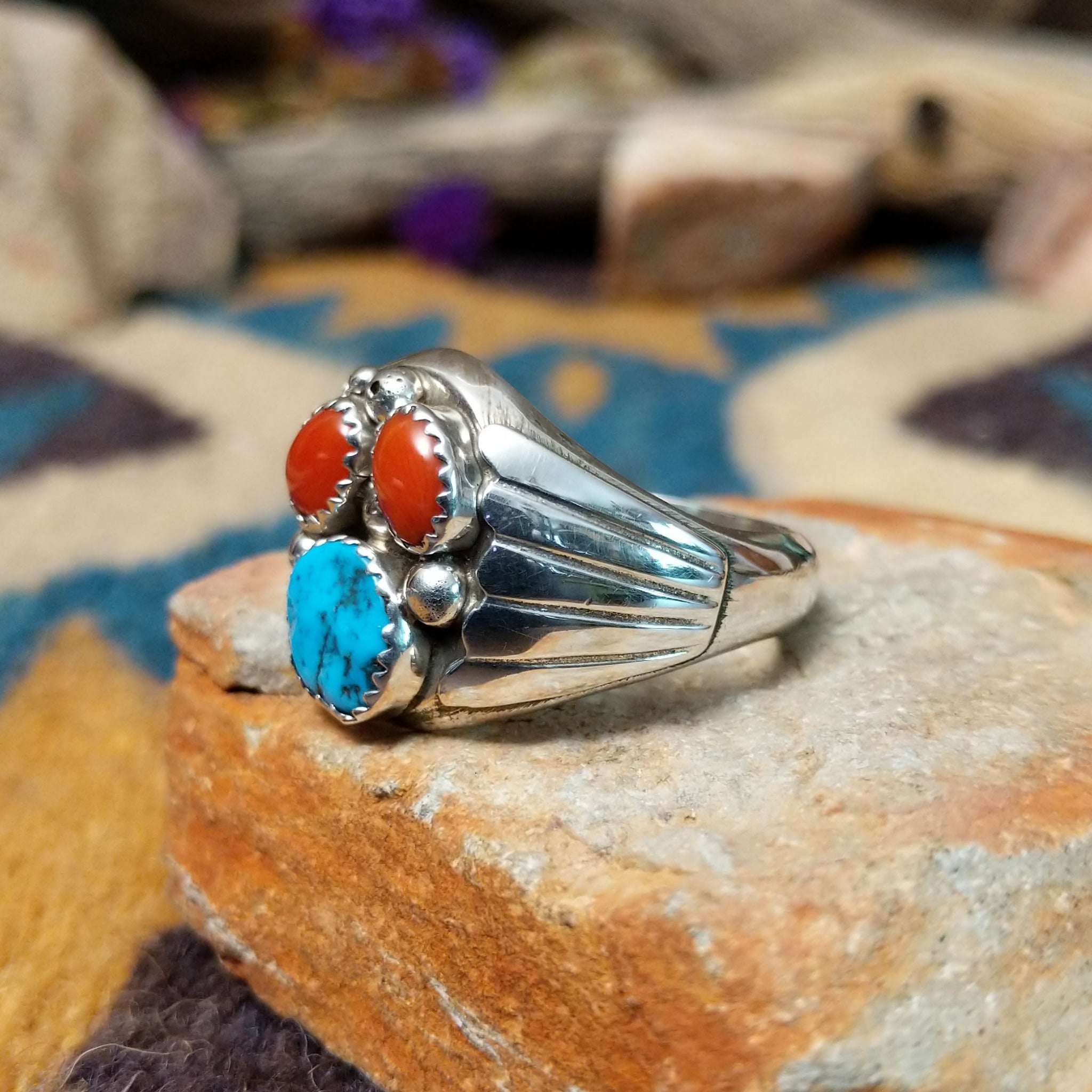 Handcrafted Navajo sterling silver ring featuring two natural red coral cabochons and one blue turquoise cabochon with traditional sawtooth bezels, silver raindrop accents, and a split-shank band; side view.