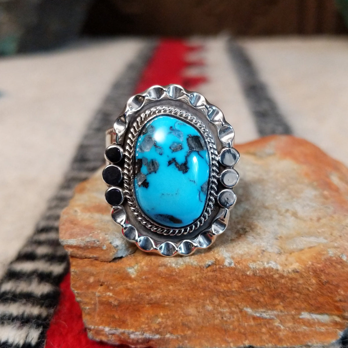 Navajo turquoise ring featuring a large oval bright blue turquoise stone with dark matrix, framed by twisted silver rope and an ornate scalloped silver setting.
