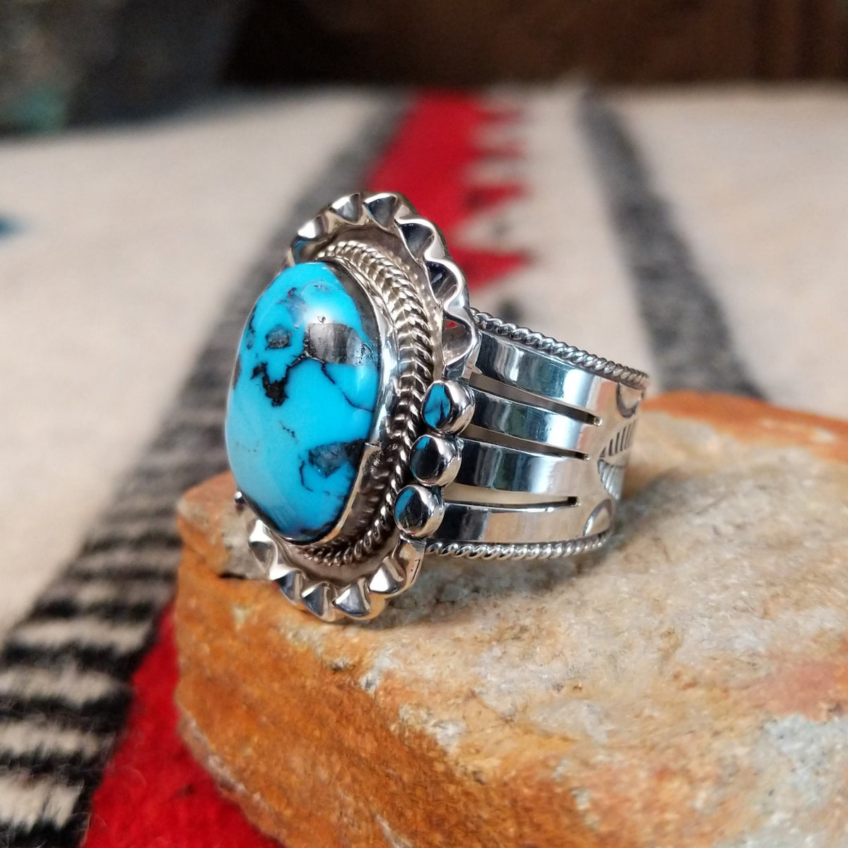 Navajo turquoise ring featuring a large oval bright blue turquoise stone with dark matrix, framed by twisted silver rope and an ornate scalloped silver setting; side view.