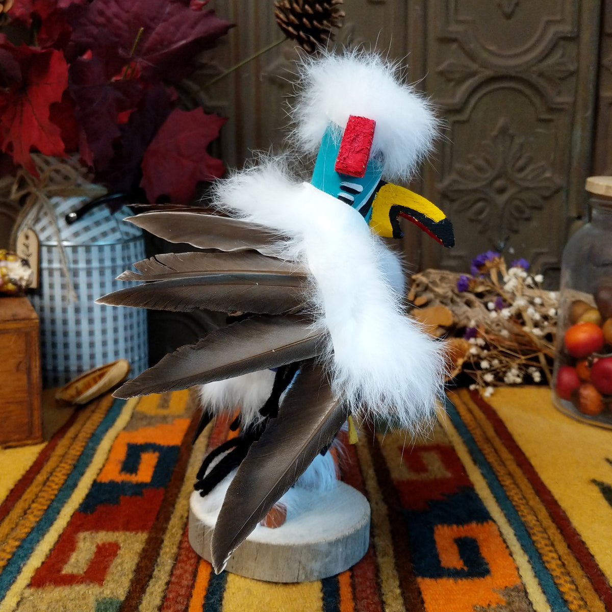 This striking Navajo Eagle Dancer Kachina by Debbie James features a colorful hand-painted eagle mask, white feather wings, fluffy headdress, leather ties, decorative clothing, and a wooden display base; side view.