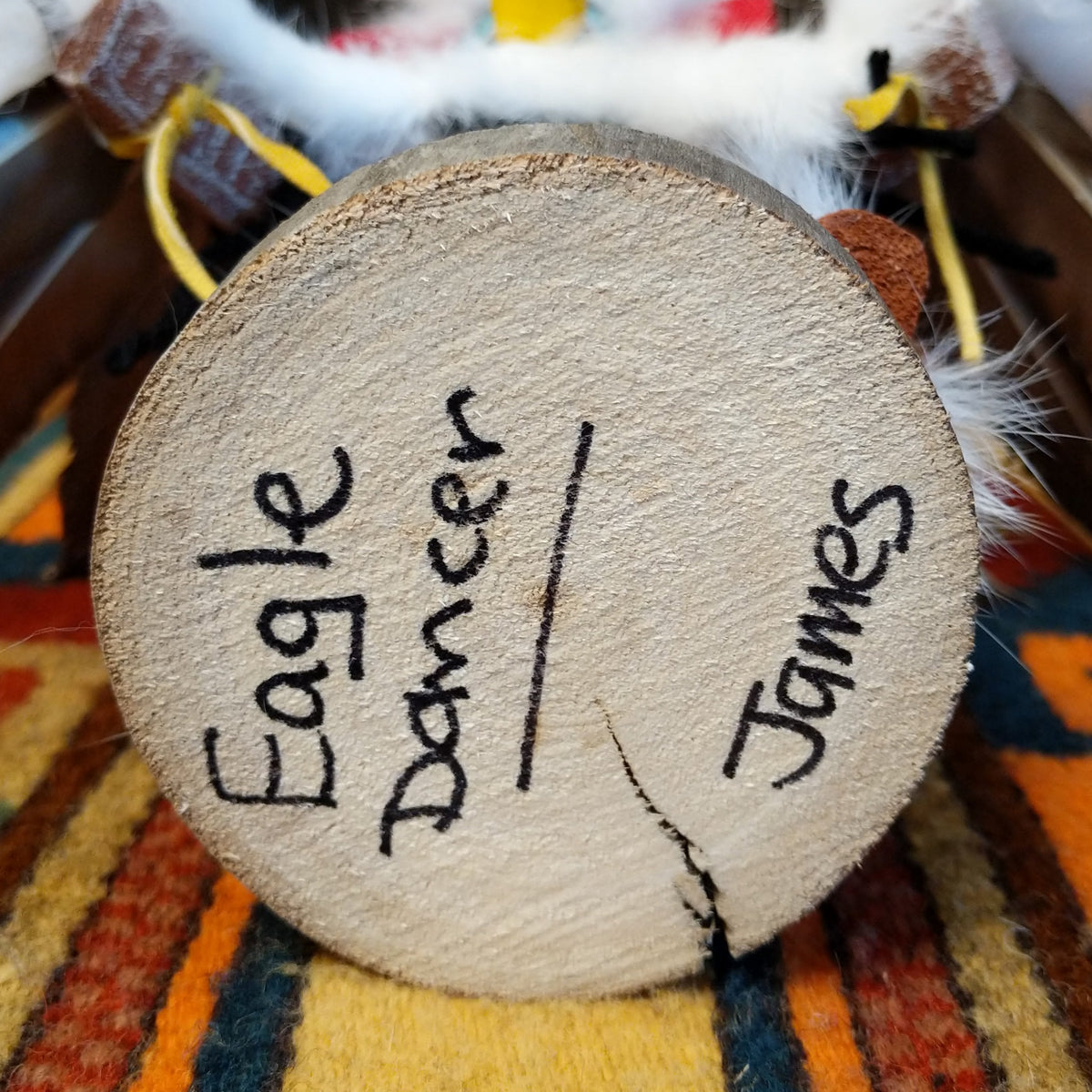 This striking Navajo Eagle Dancer Kachina by Debbie James features a colorful hand-painted eagle mask, white feather wings, fluffy headdress, leather ties, decorative clothing, and a wooden display base; artisan and product name on bottom.
