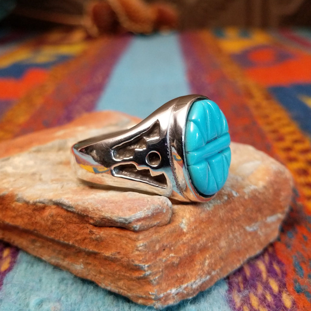 Navajo Etched Turquoise Ring featuring an oval turquoise stone carved with symmetrical geometric triangular patterns and a raised horizontal bar, set in a polished silver band with openwork side details; side view.