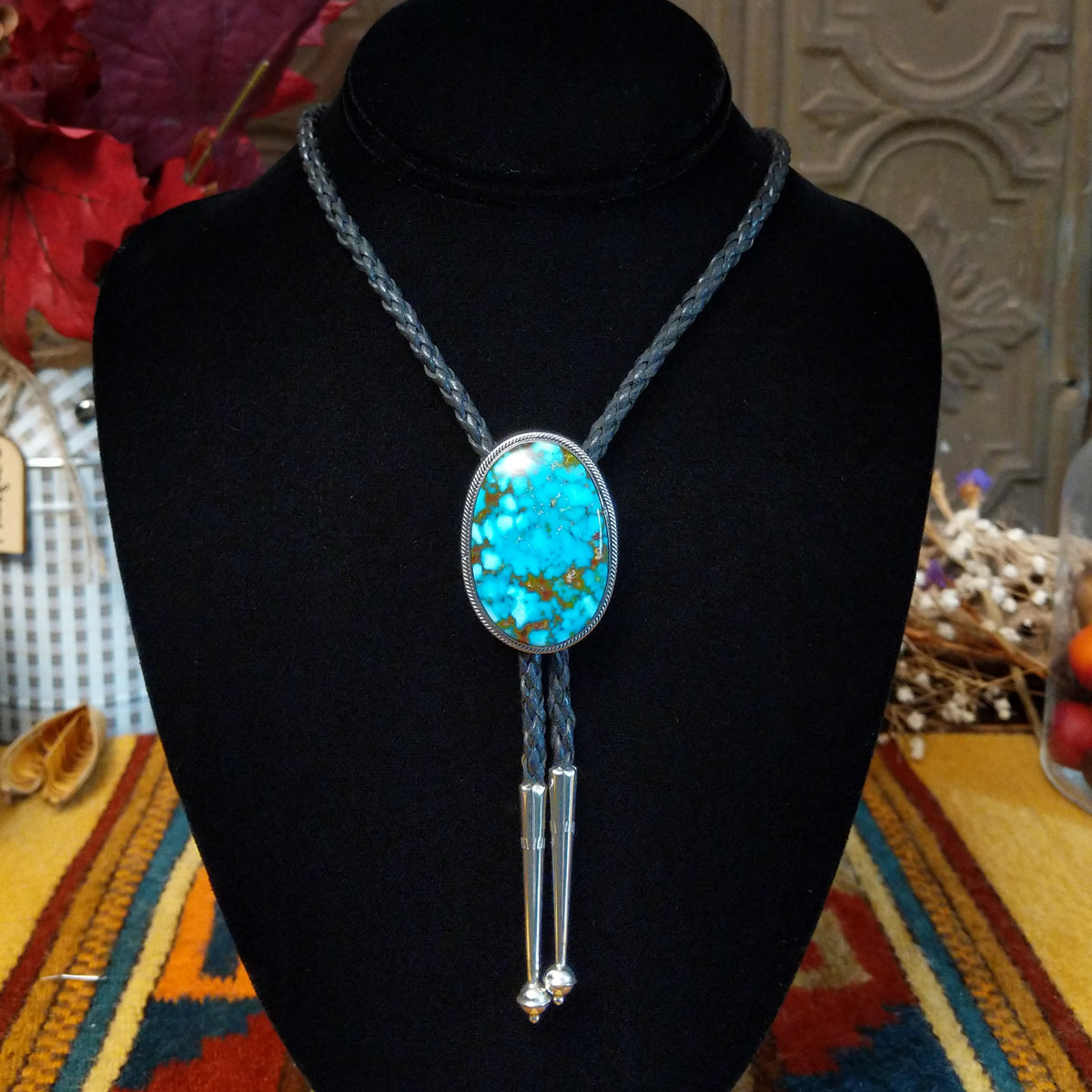 Navajo Kingman Turquoise Bolo Tie featuring a large oval sky-blue turquoise stone with golden-brown matrix, decorative silver bezel, braided black leather cord, and polished silver tips.