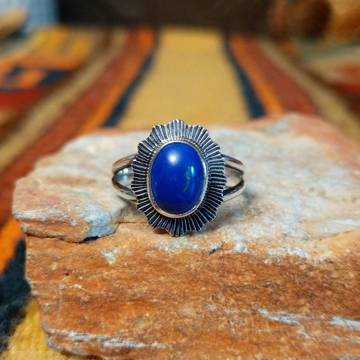 Front view of a silver ring with an oval cobalt-blue lapis lazuli stone framed by a scalloped, sunburst-patterned silver setting.