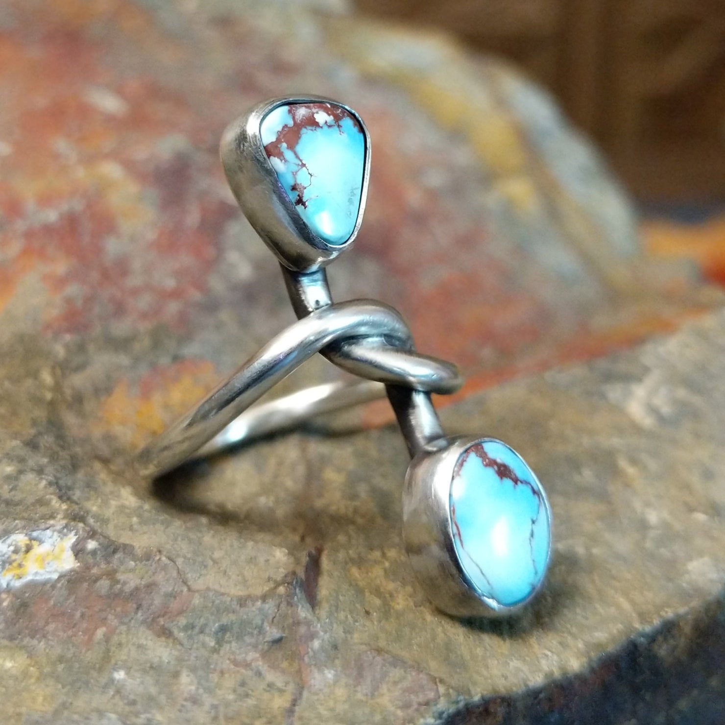 Silver ring with entwined band showing a triangular and oval turquoise stone with matrix veining visible.