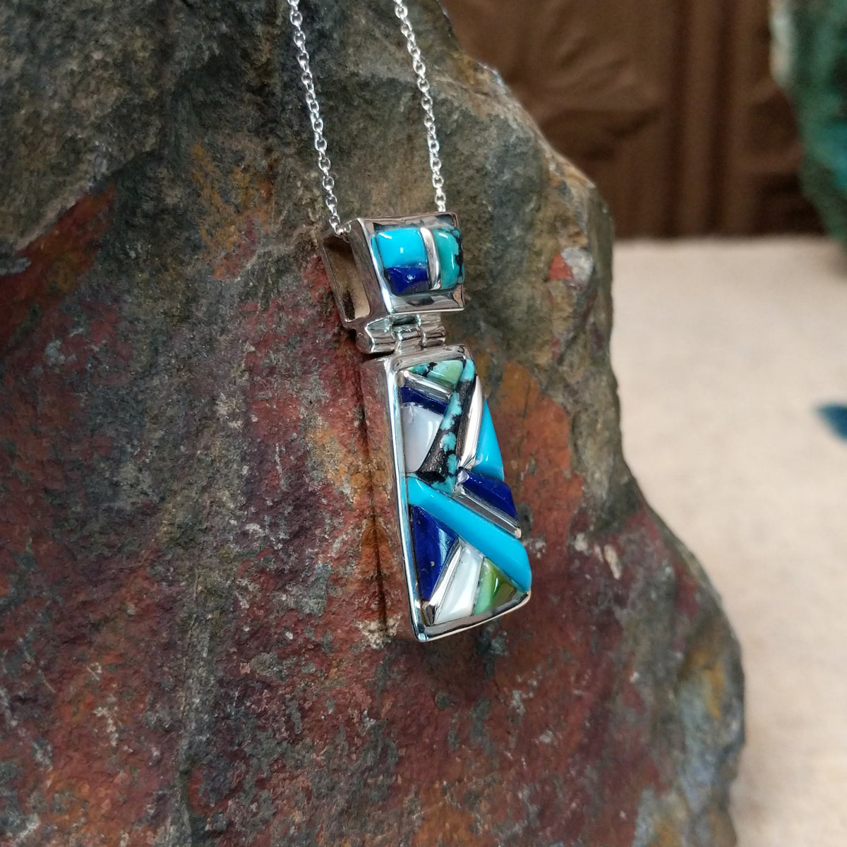 Navajo multistone cobblestone inlay pendant by J.Y. featuring turquoise, lapis, black matrix turquoise, white, and green stone inlay in a geometric sterling silver design; side view.
