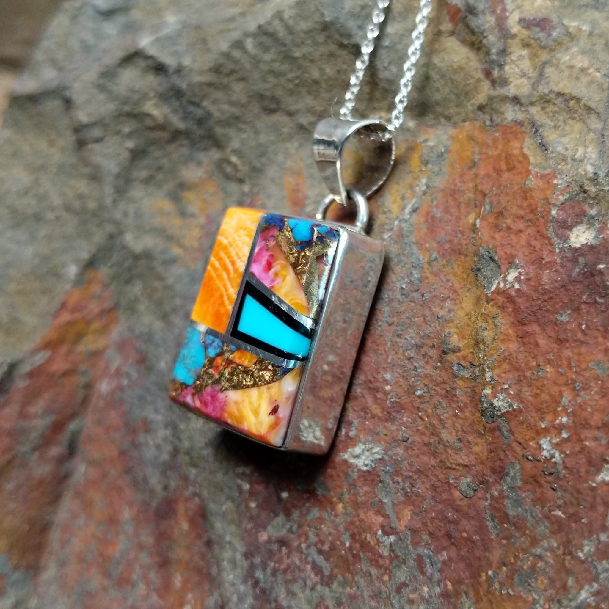 Handcrafted sterling silver compressed stone inlay pendant by S.L., featuring a colorful geometric Navajo design; side view.