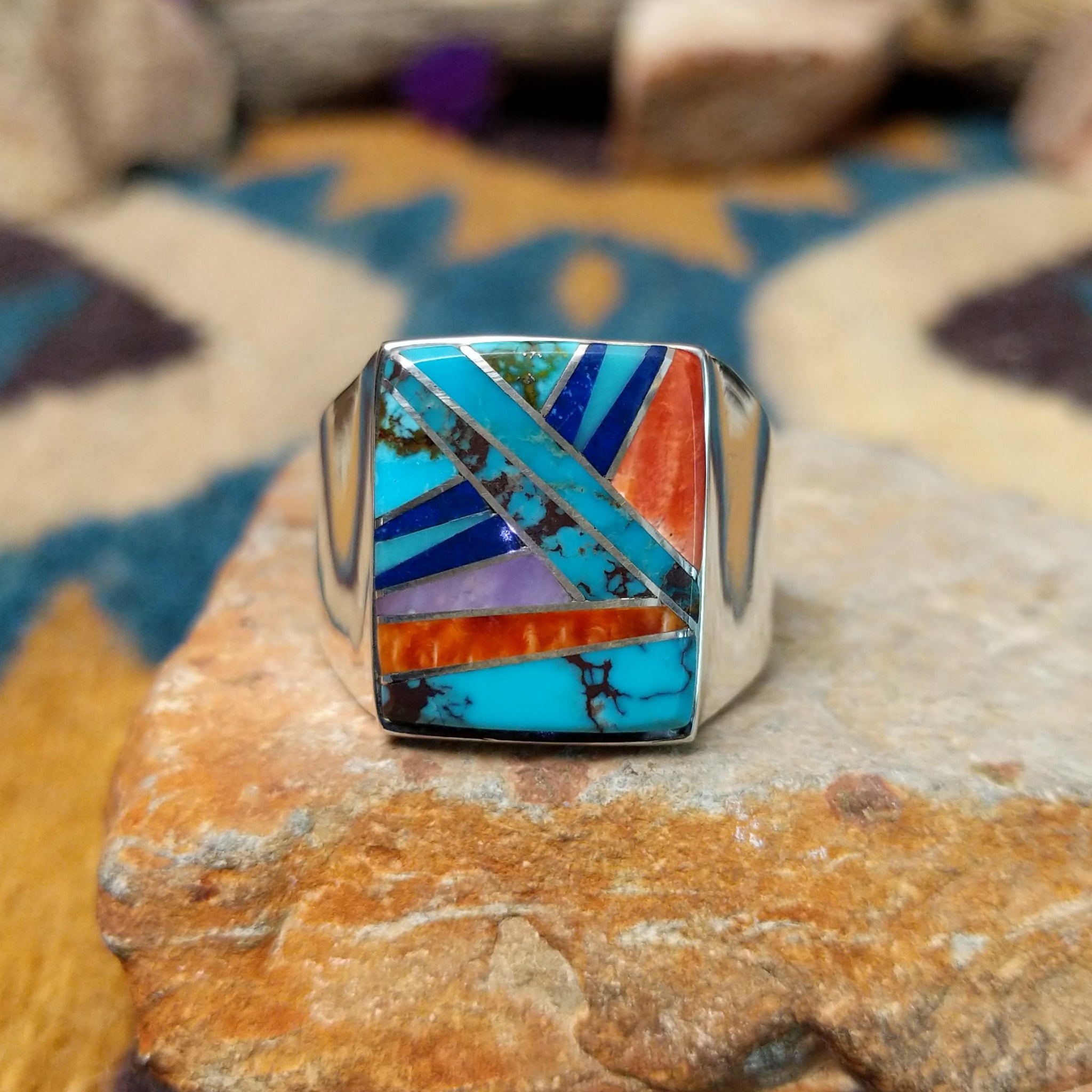 Sterling silver Navajo multistone inlay ring featuring turquoise, orange spiny oyster shell, lapis, and geometric mosaic inlay on a polished signet-style band.