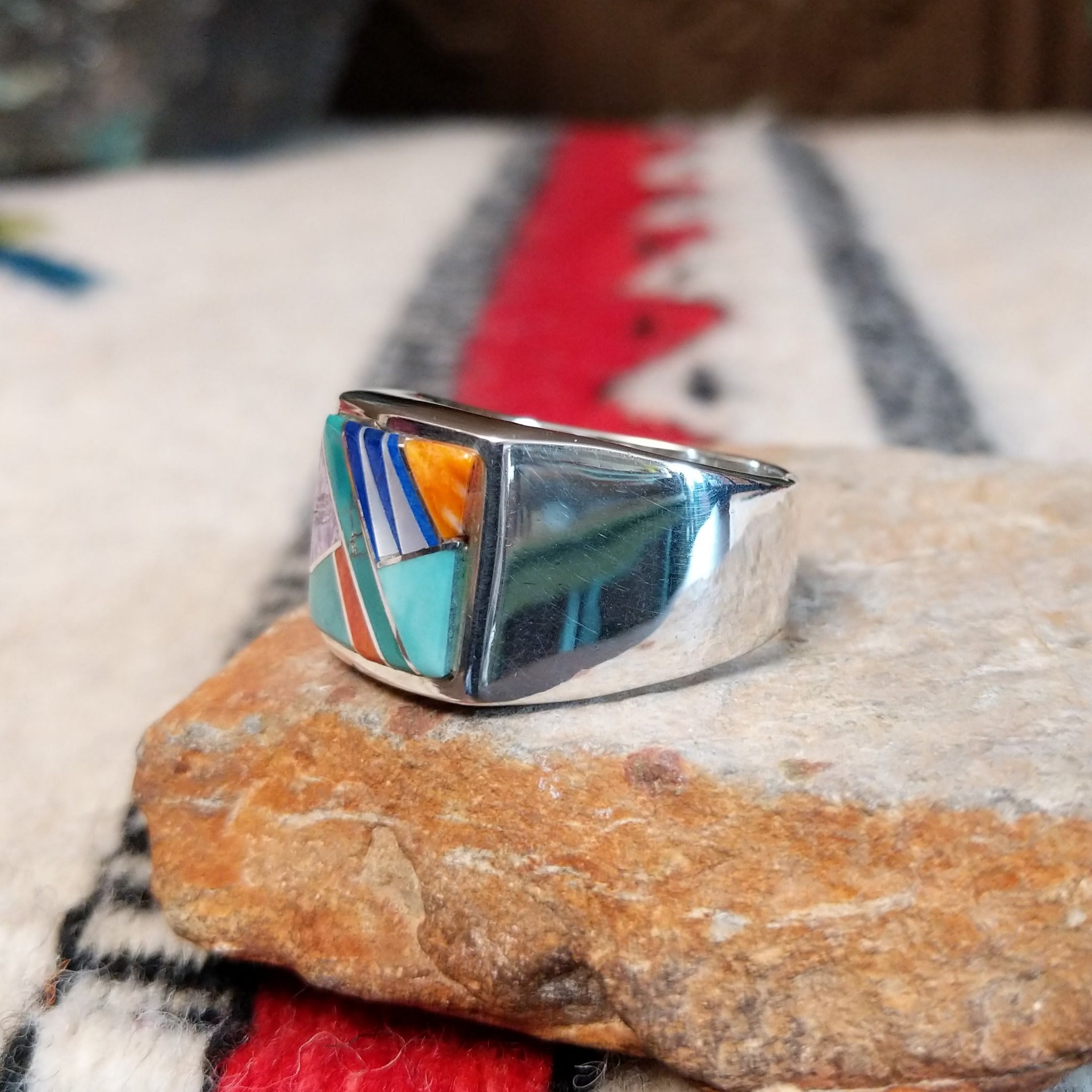 Navajo Multistone Inlay Ring by A.M.P. featuring a square geometric mosaic of turquoise, blue, purple, orange, red, and iridescent inlay set in a wide polished silver band; side view.