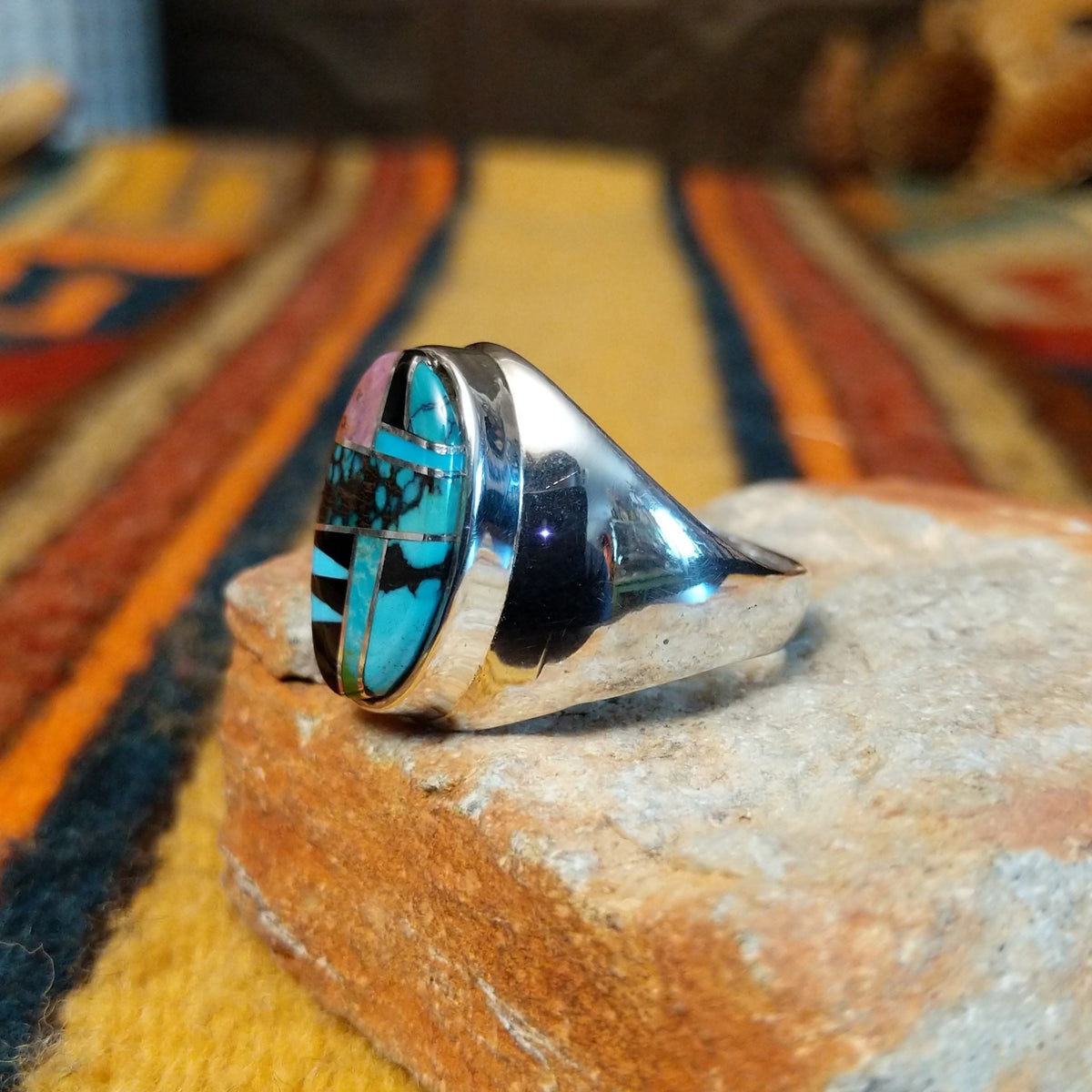 Navajo Multistone Inlay Ring by P.D. featuring an oval geometric mosaic of turquoise, black onyx, and contrasting stone inlays separated by thin silver dividers, set in a wide, polished silver band; side view.