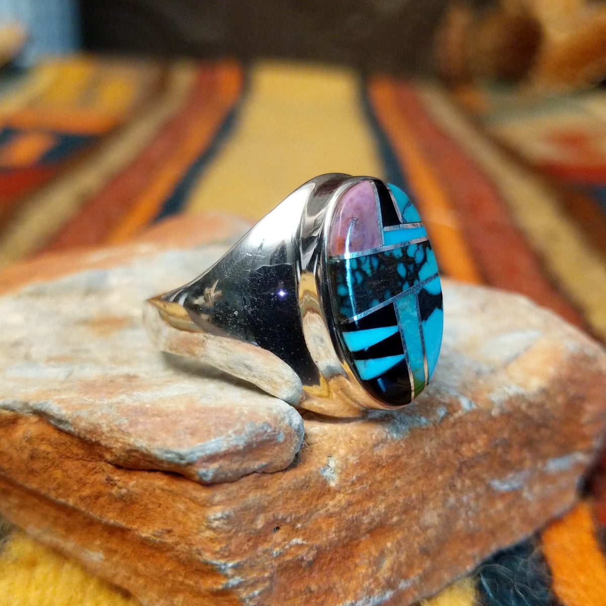 Navajo Multistone Inlay Ring by P.D. featuring an oval geometric mosaic of turquoise, black onyx, and contrasting stone inlays separated by thin silver dividers, set in a wide, polished silver band; side view.
