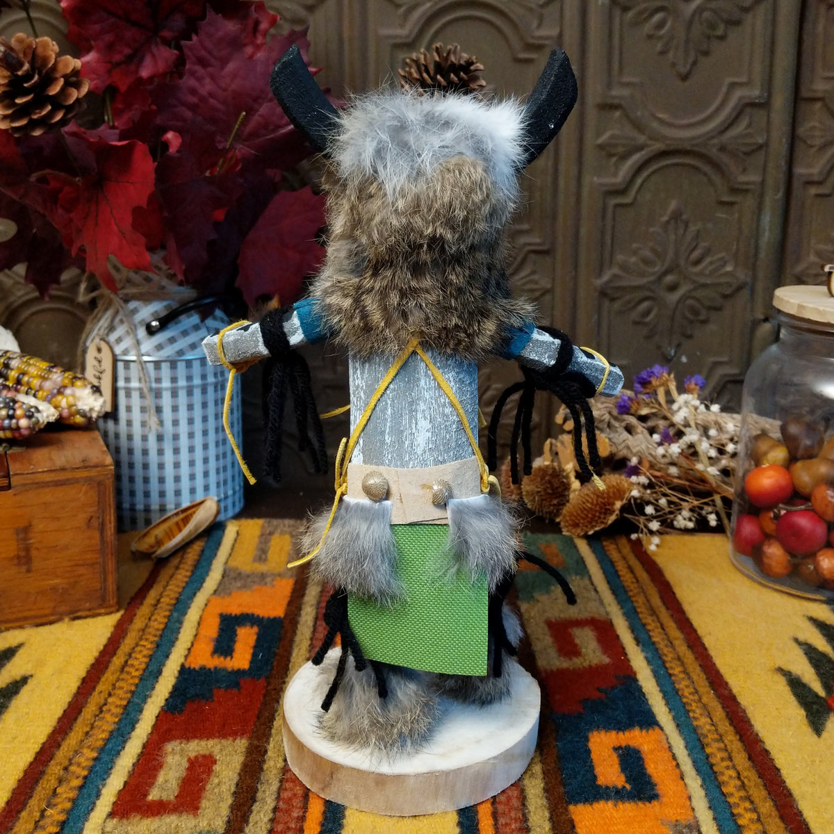 Back view of the Navajo Ogre Kachina doll with gray fur-covered face, black horns with turquoise markings, open red mouth, pointed teeth, and green fabric apron.
