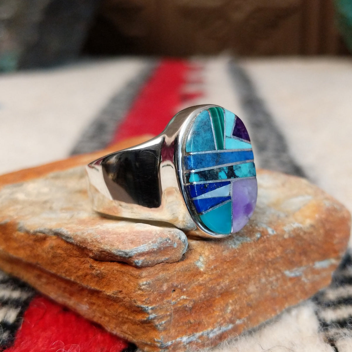 Navajo oval multistone inlay ring by E.D. featuring turquoise, blue, green, and purple stones arranged in a geometric mosaic with silver channel accents and a polished silver band; side view.