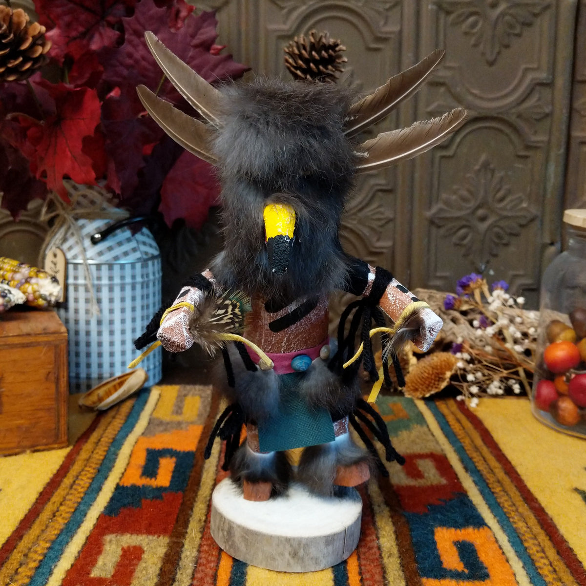 This unique Navajo Owl Kachina by Debbie James features a hand-painted wooden figure with a yellow and black owl beak, dark fur headdress, natural feathers, leather ties, decorative clothing, and a wooden display base.