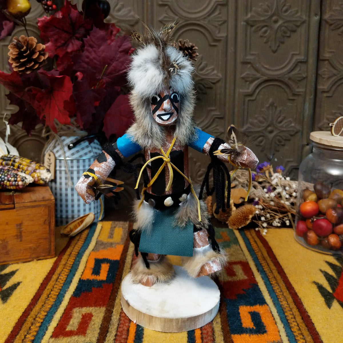 Navajo Protection Dancer Kachina doll with gray fur headdress, black painted facial markings, blue sleeves, feather accents, and raised foot.