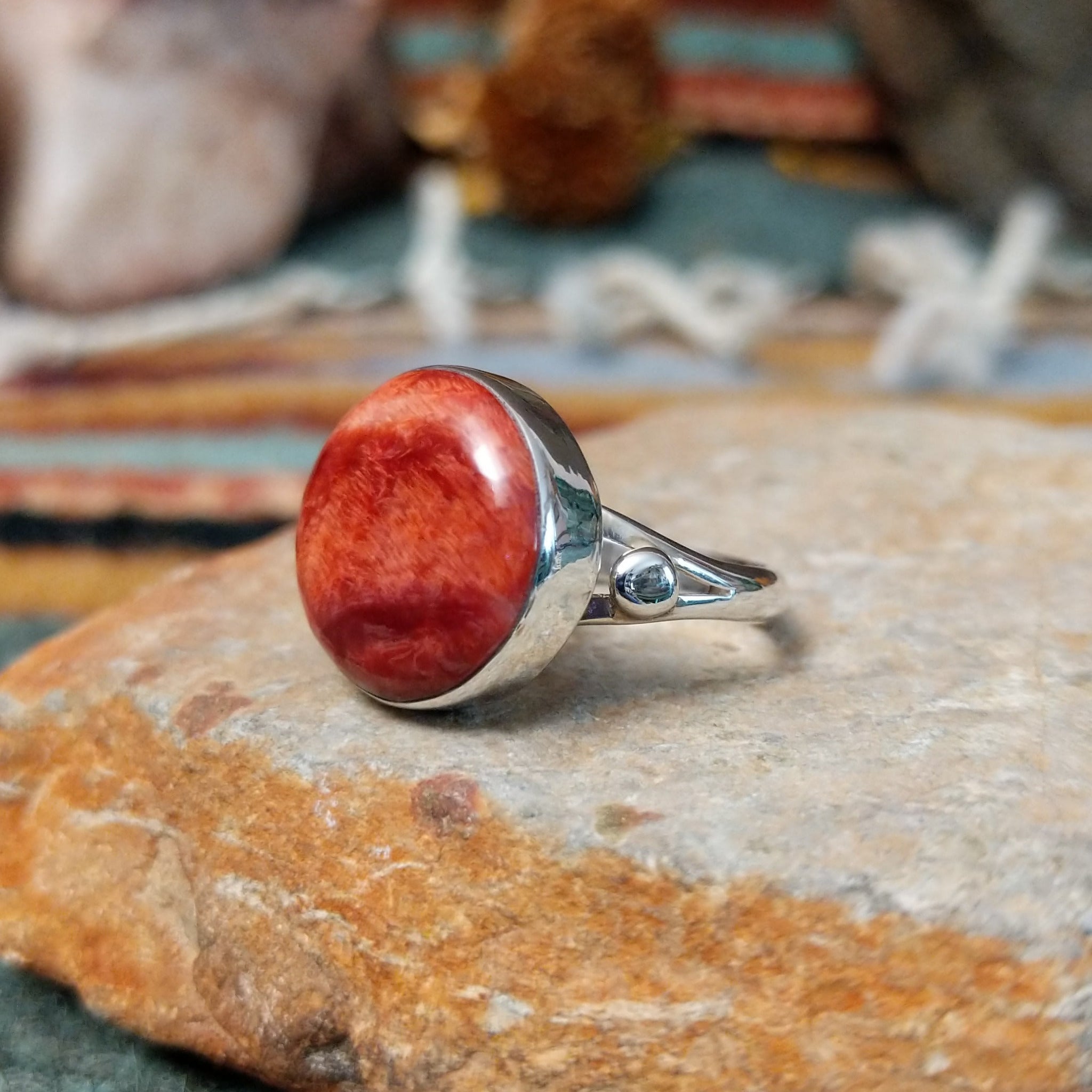 Navajo sterling silver ring by N.A. featuring a round red spiny oyster shell cabochon with natural color variations in a smooth silver bezel; side view.