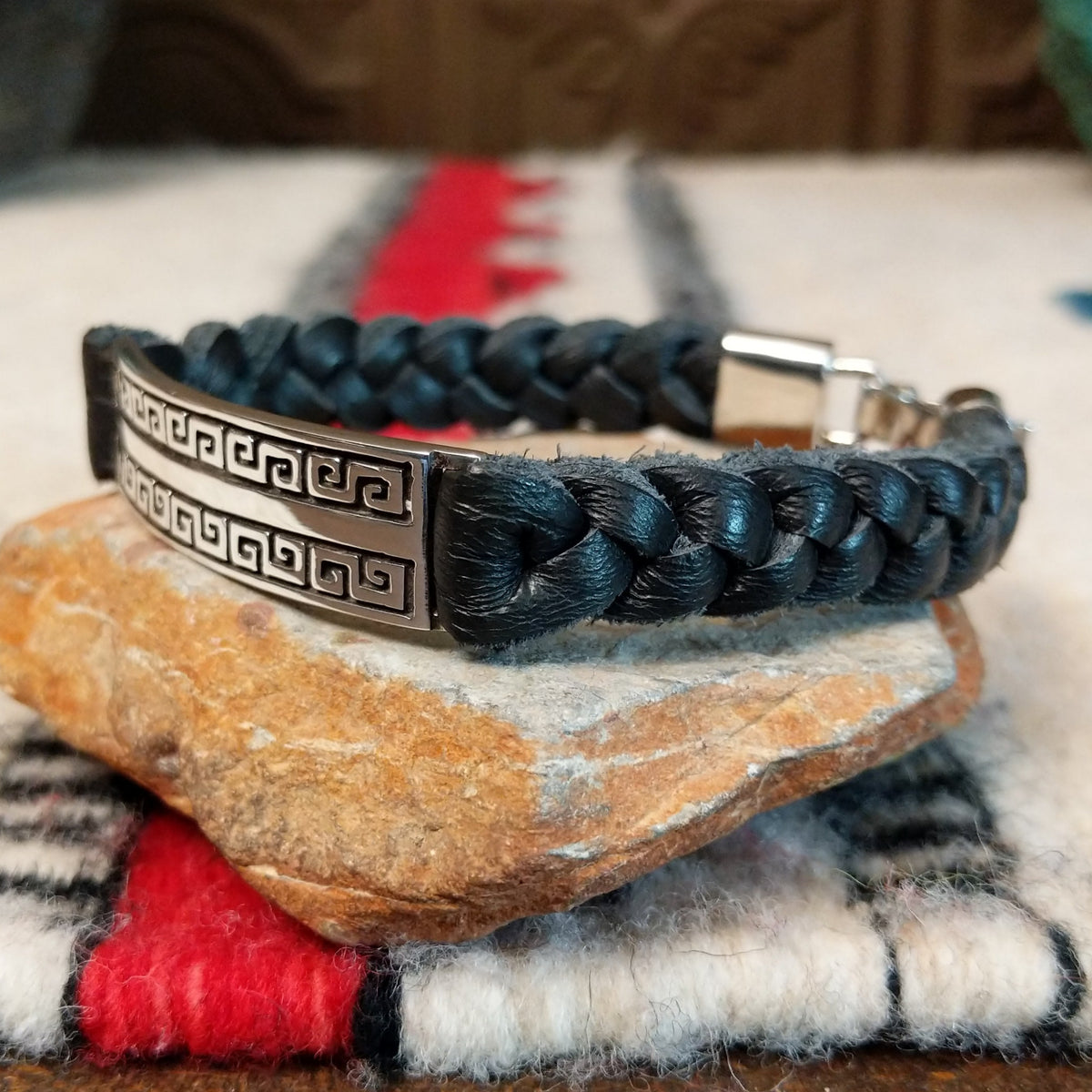 Navajo bracelet featuring braided black leather and a rectangular silver centerpiece with two rows of repeating geometric scroll patterns and darkened recessed details; side view.