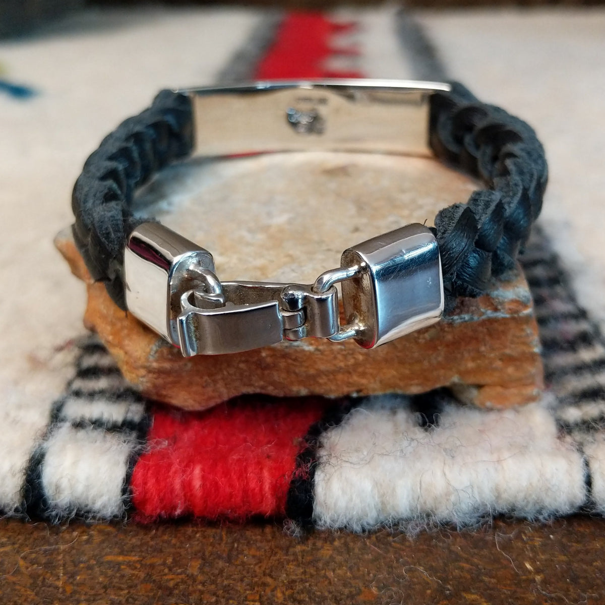 Navajo bracelet featuring braided black leather and a rectangular silver centerpiece with two rows of repeating geometric scroll patterns and darkened recessed details; clasp view.