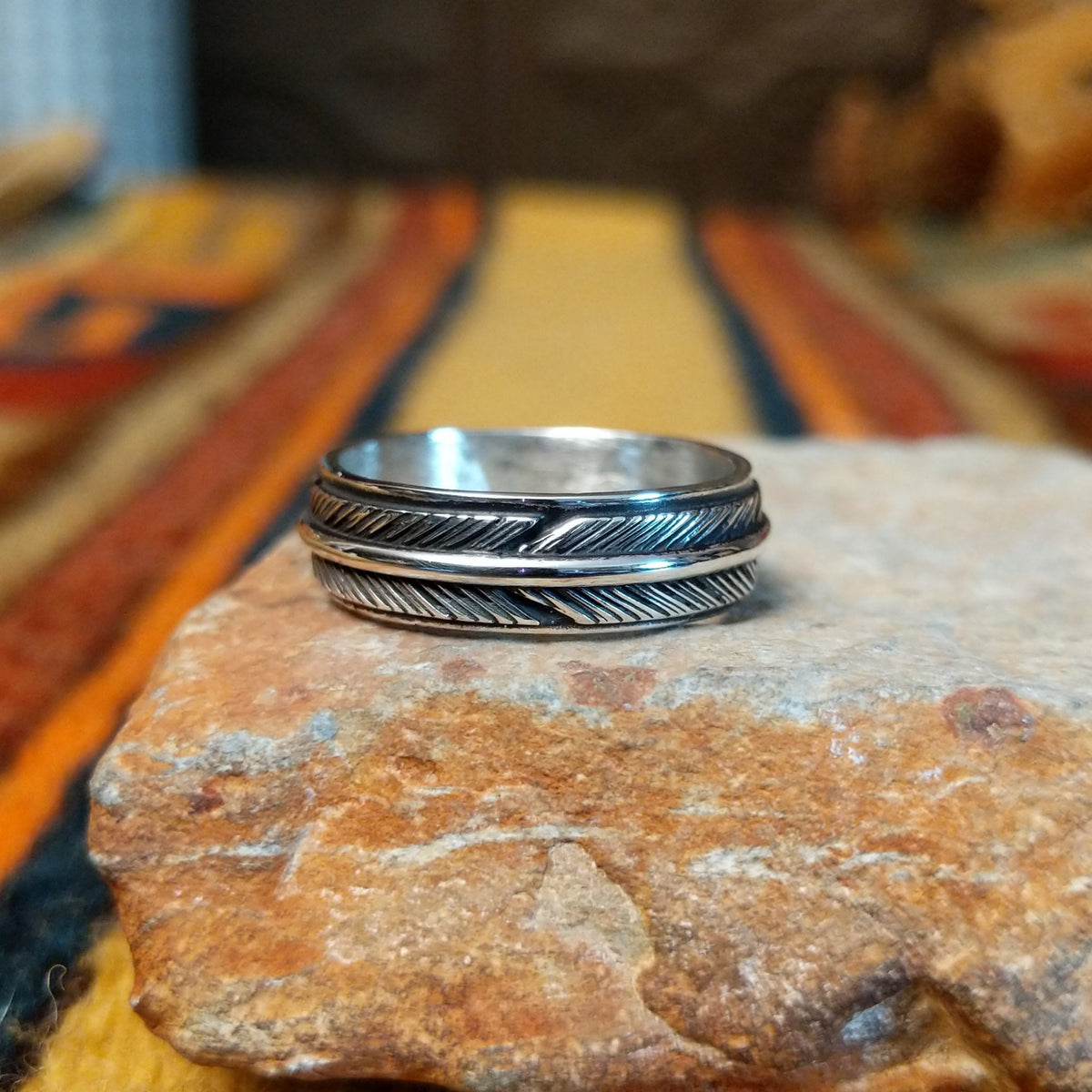 Silver feather-patterned band ring featuring diagonal engraved lines, darkened recesses, and a raised polished silver ridge around the center.
