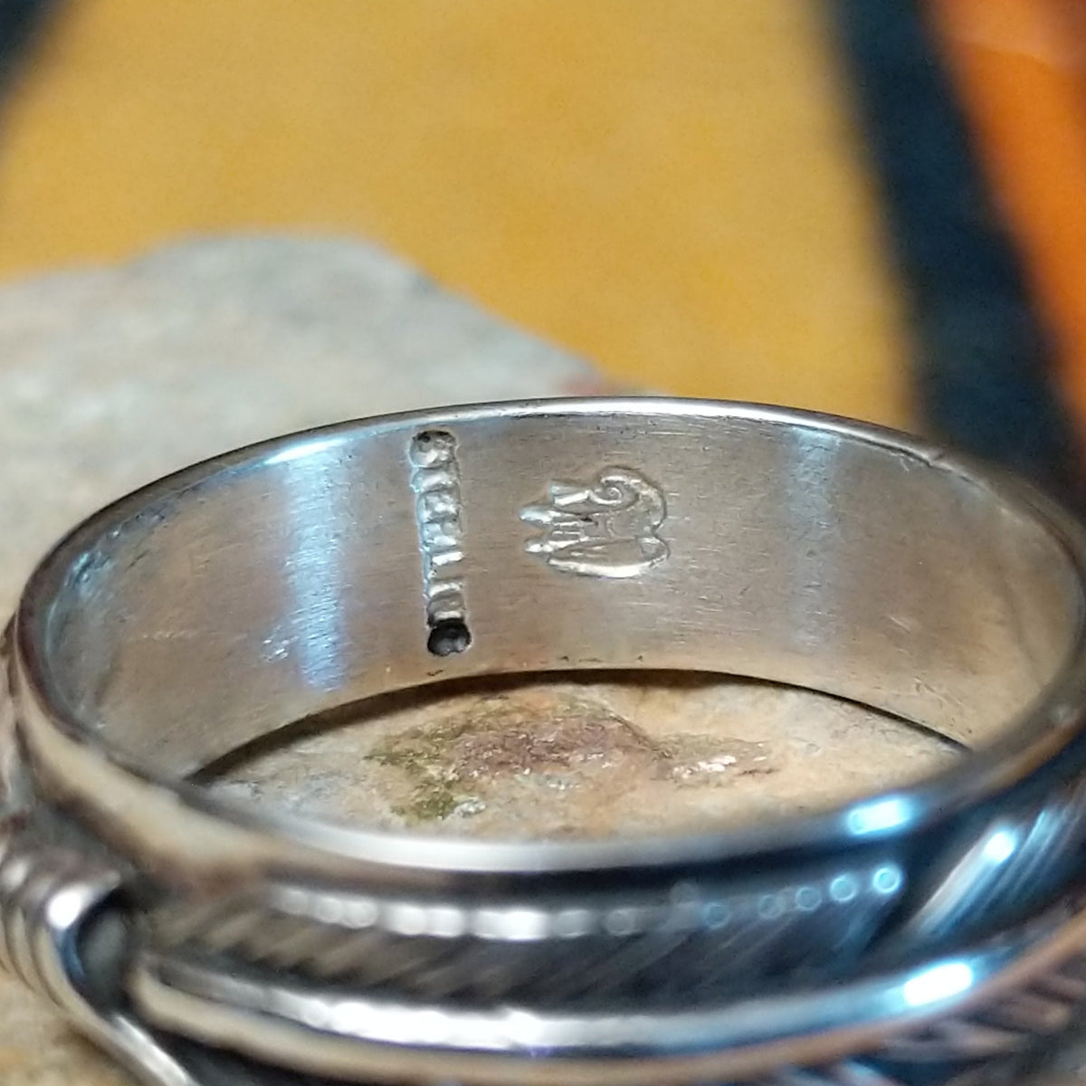 Close-up of the inside of a silver feather-patterned ring showing a vertical sterling stamp and a stamped hallmark.