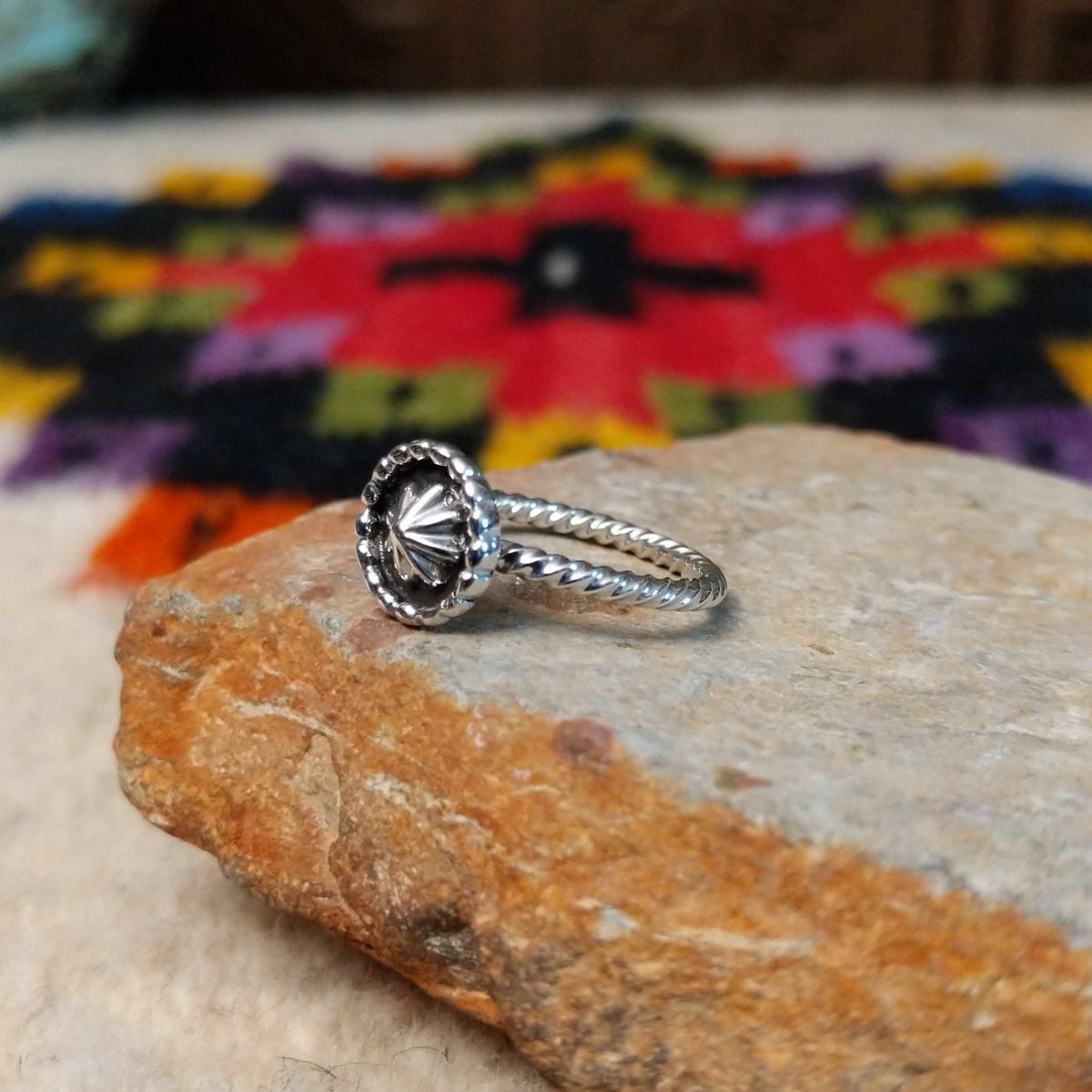 This Navajo Silver Star Ring features a round sterling silver face with a polished starburst design, dark oxidized background, beaded border, and textured silver band; side view.