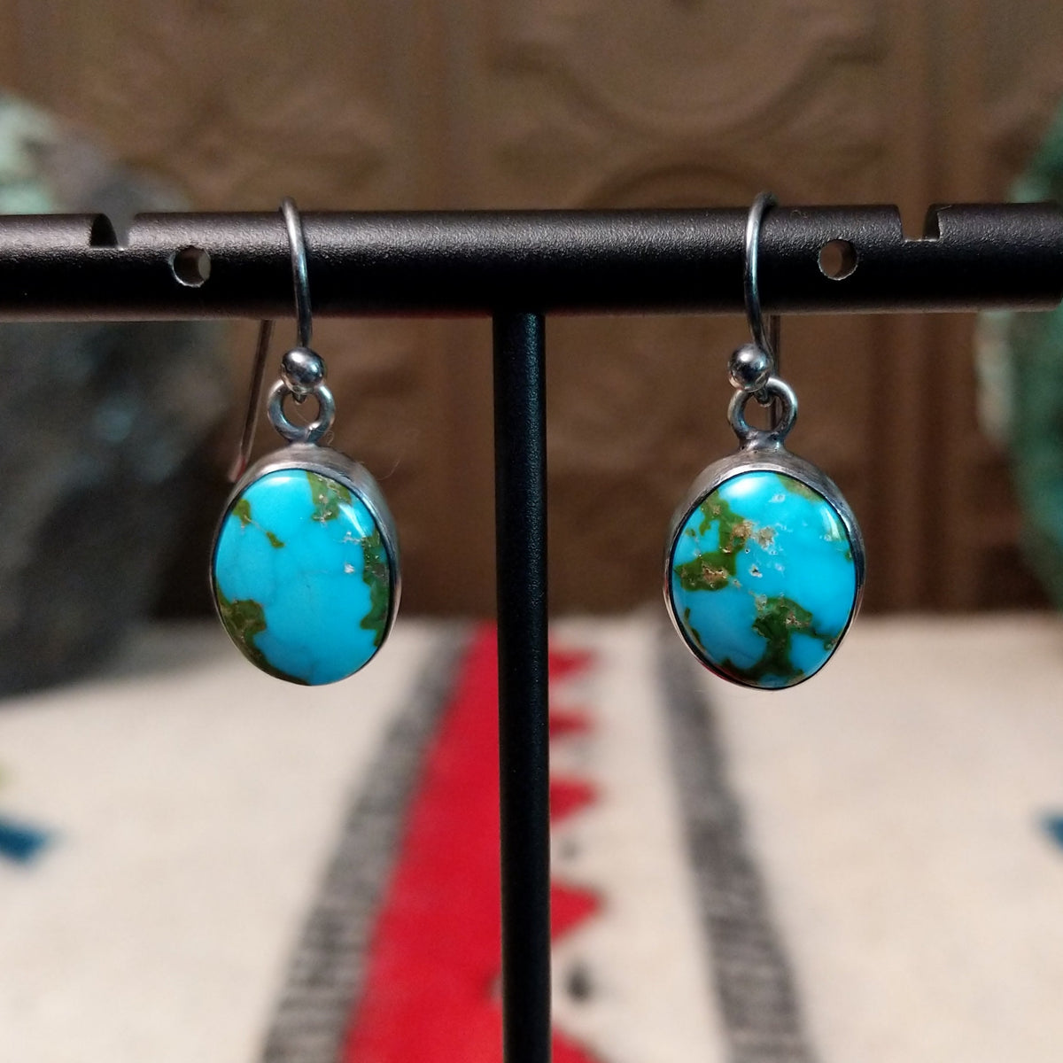Navajo Sonoran Gold turquoise earrings by J.P. featuring oval bright blue turquoise stones with green and earthy matrix, smooth sterling silver bezels, and French wire hooks.