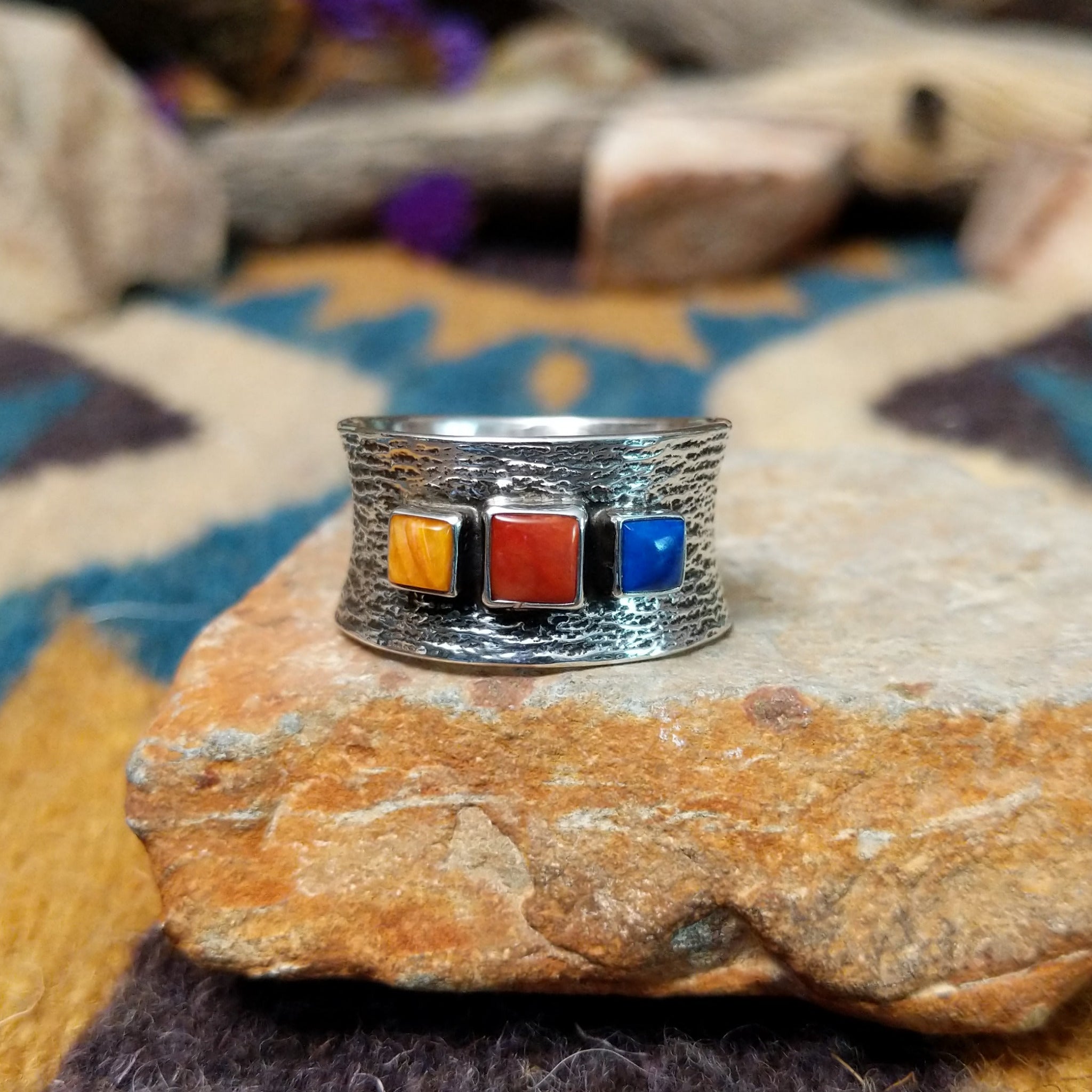 Navajo sterling silver textured band ring with three square gemstones in yellow, red, and blue.