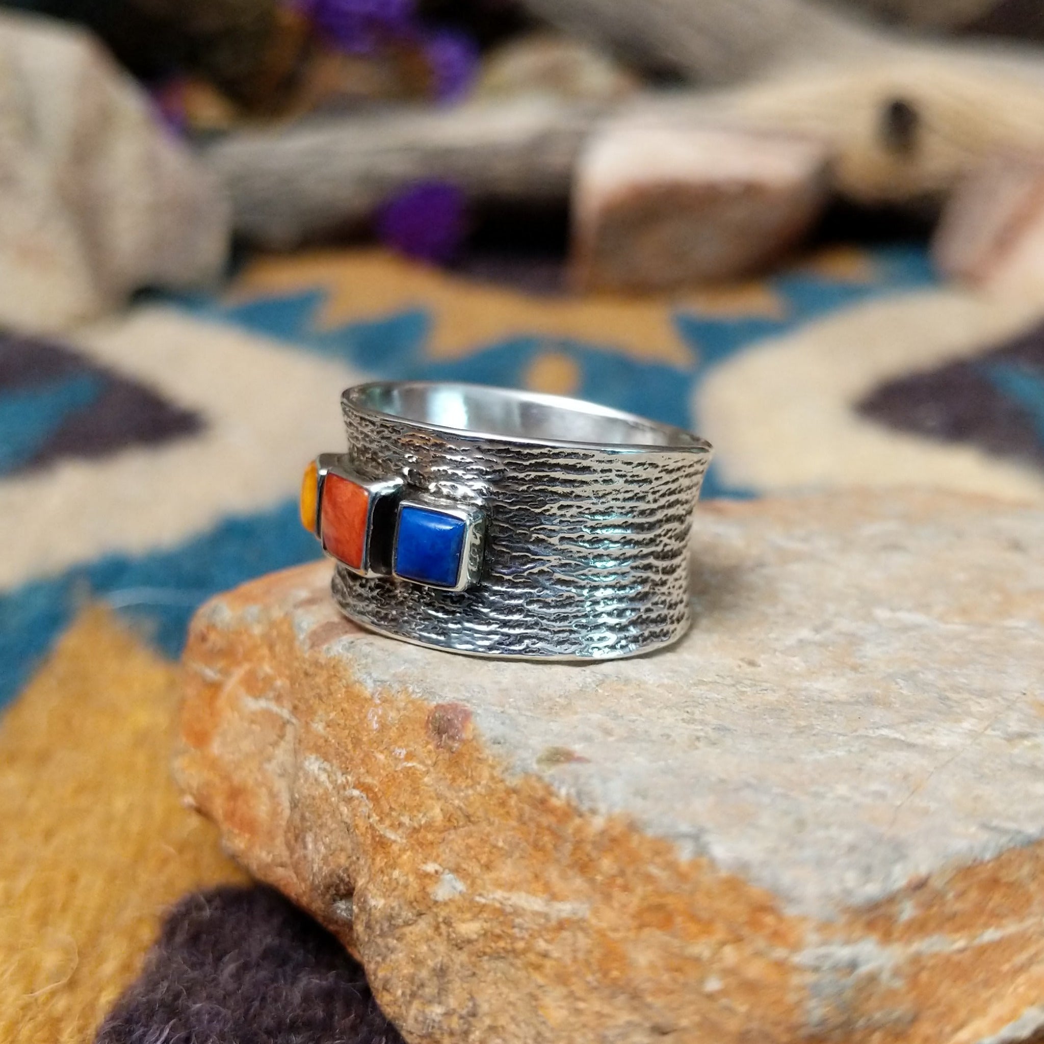 Navajo sterling silver textured band ring with three square gemstones in yellow, red, and blue; side view.