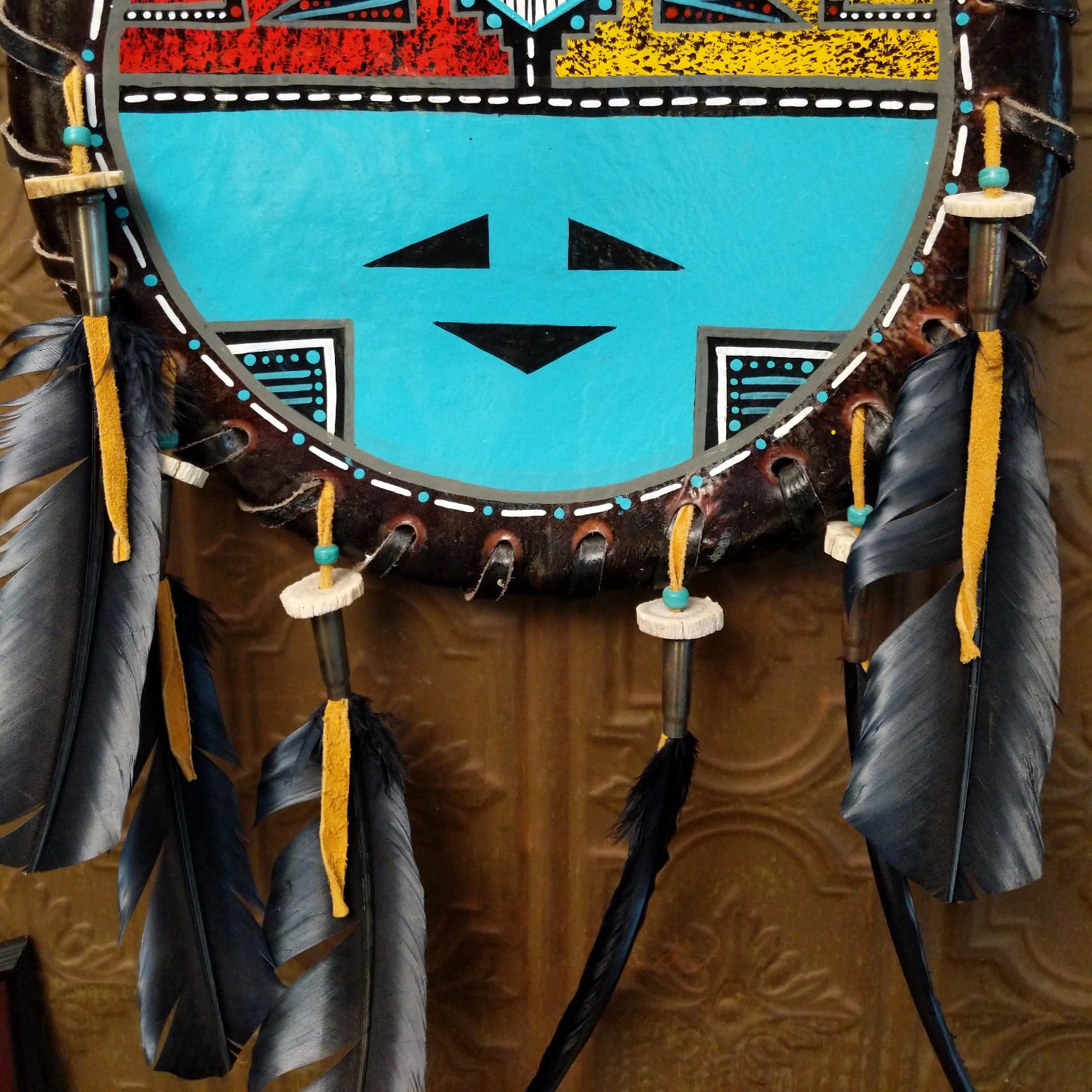 Close-up of the painted turquoise face of the piece and the feathers tethered to leather.