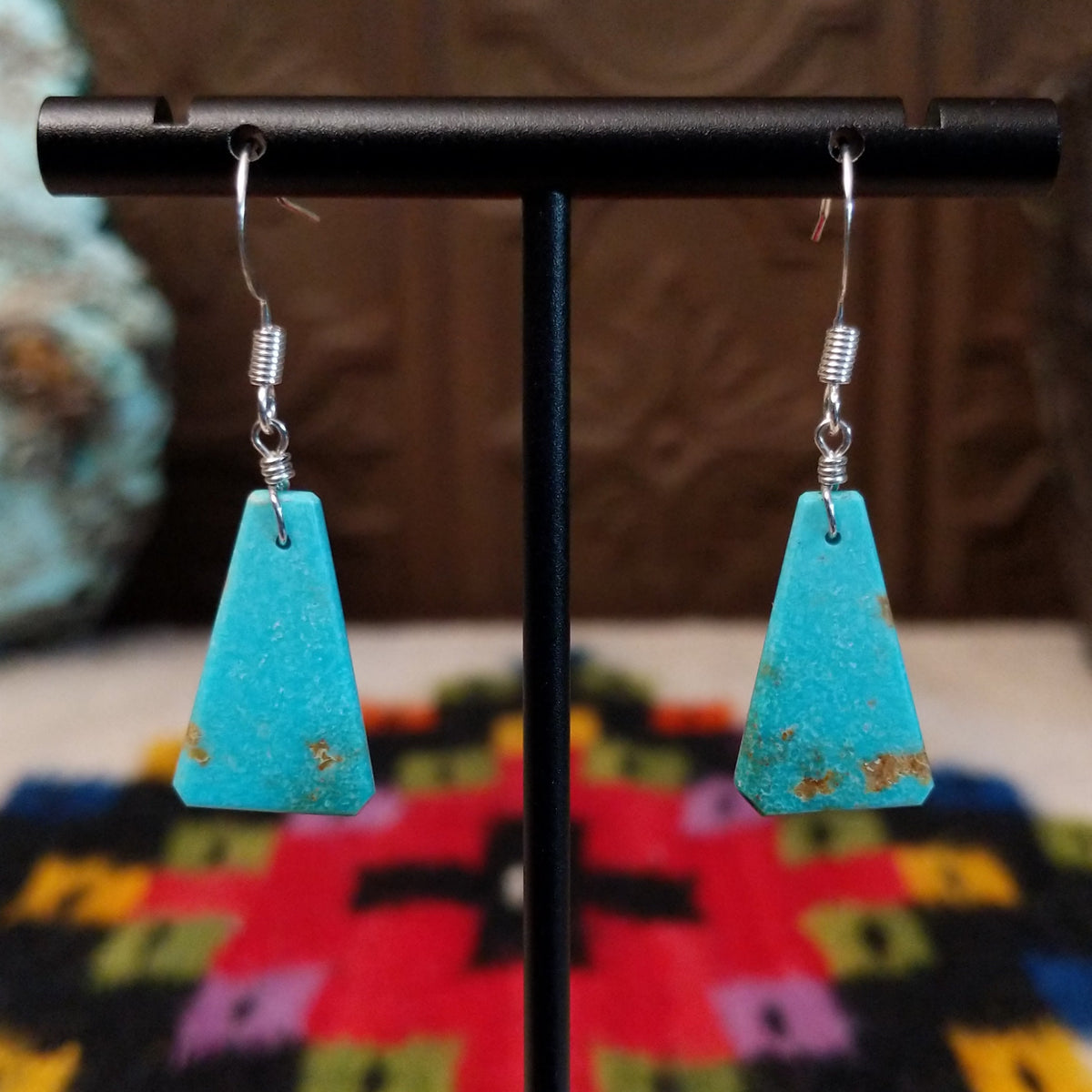 Navajo triangular turquoise slab earrings featuring bright blue stones with subtle tan and brown matrix, suspended from silver hooks.