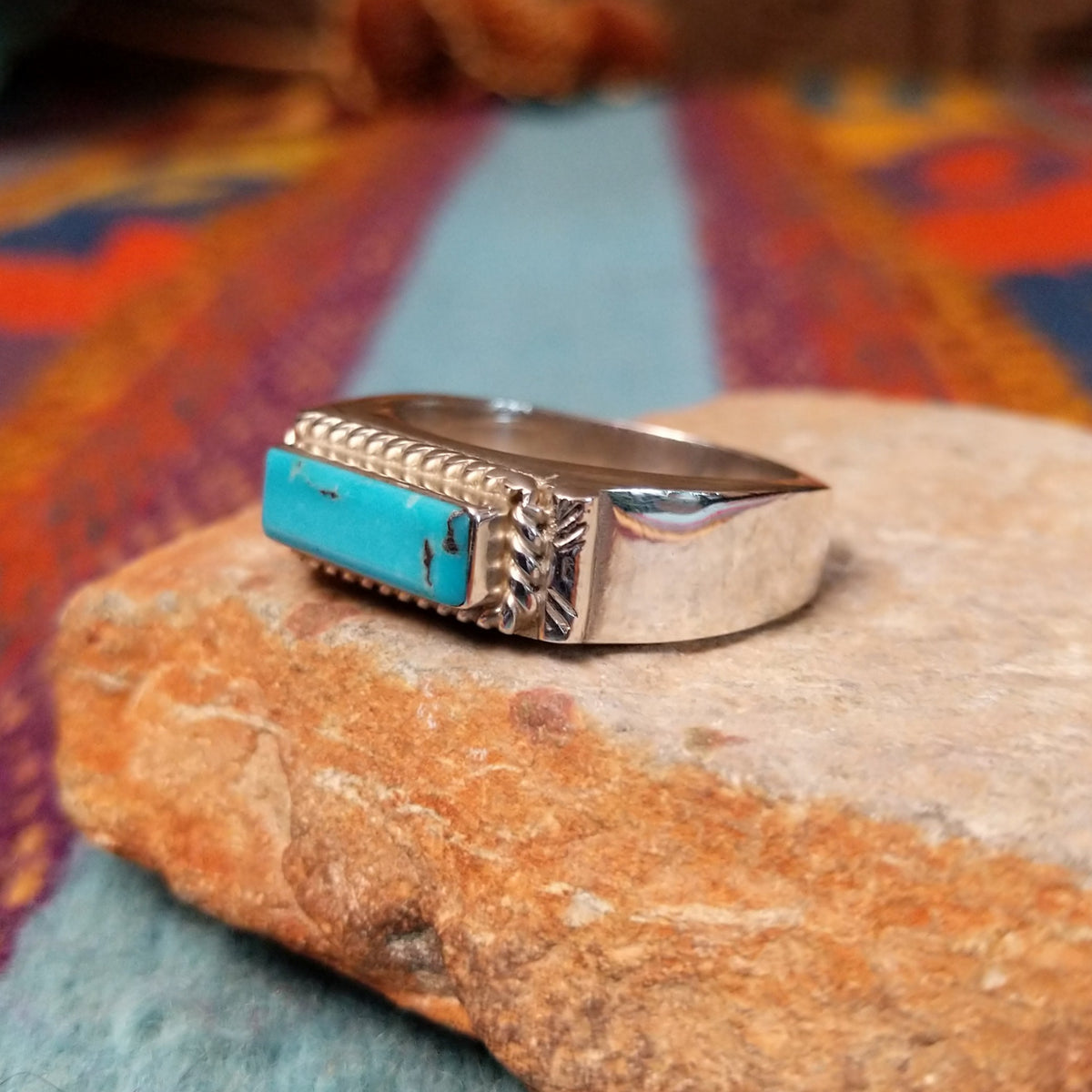 Navajo Turquoise Bar Ring by A.Q.J. featuring a rectangular bright blue turquoise stone with subtle matrix, framed by twisted-rope silverwork and decorative stamped details; side view.