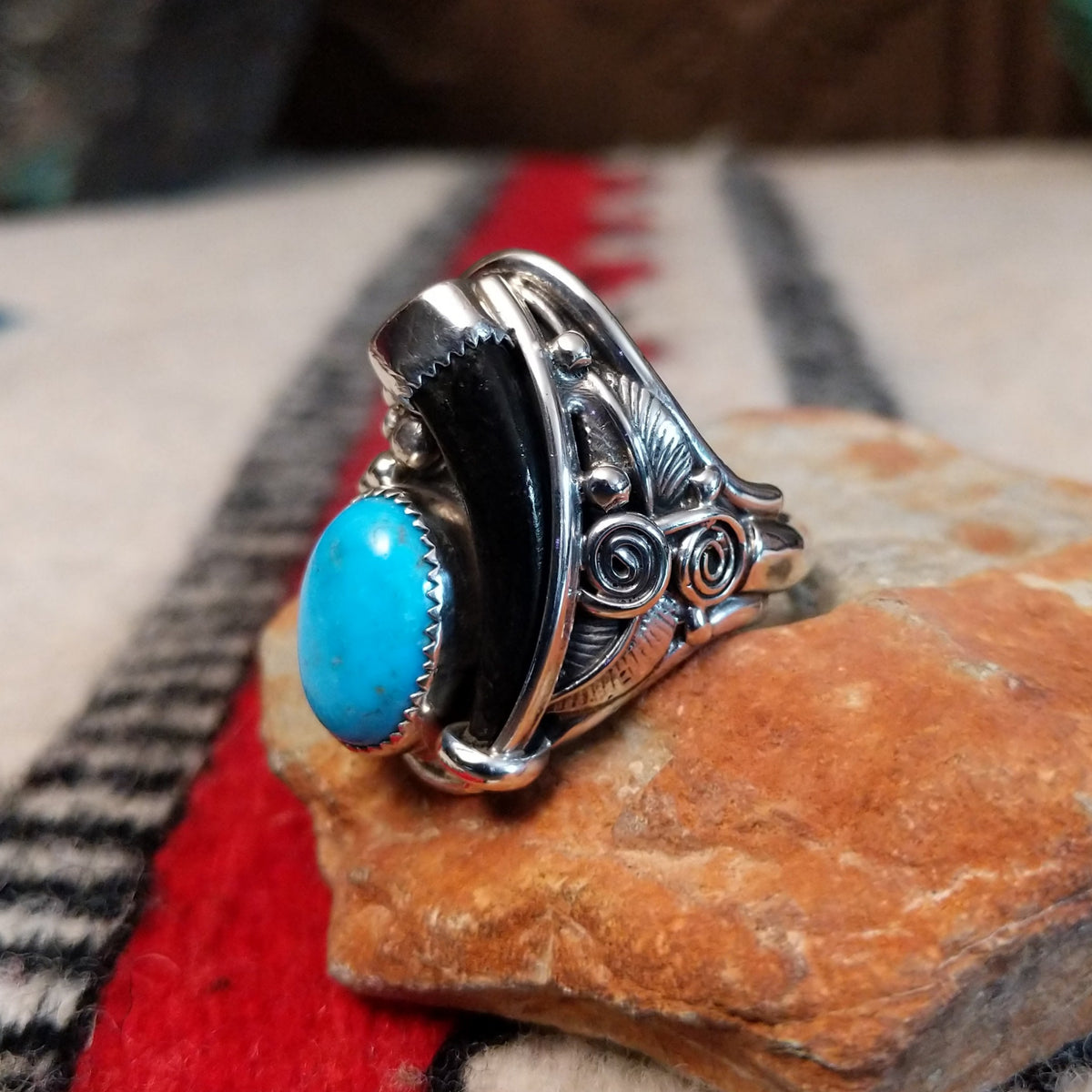 Navajo silver ring featuring a dark bear claw, oval turquoise stone, and detailed feather, scroll, and bead-style silverwork in an elongated statement design; side view.