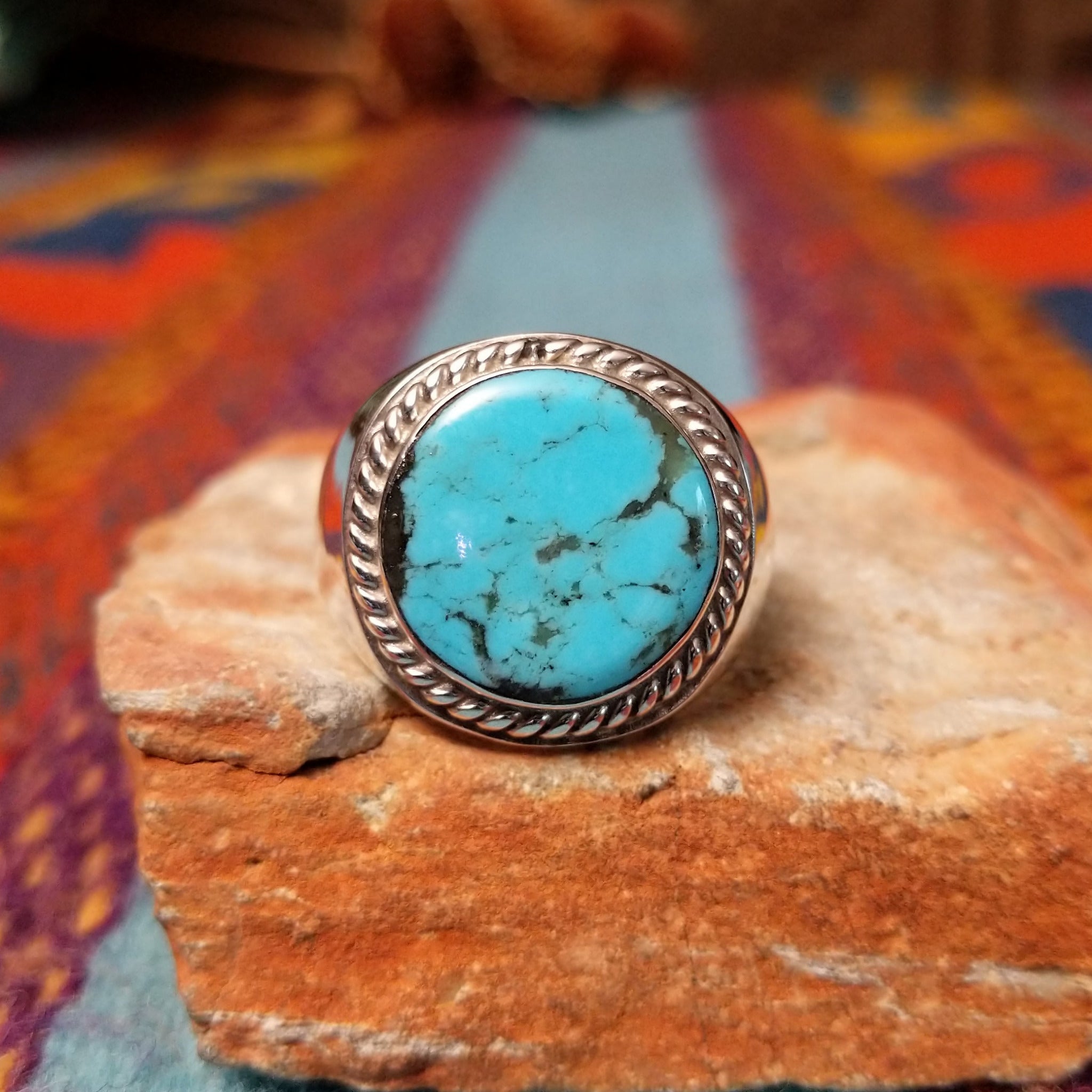 Navajo Turquoise Circle Ring by A.Q.J. featuring a large round turquoise stone with natural dark matrix, framed by twisted rope detailing and set in polished Sterling Silver.
