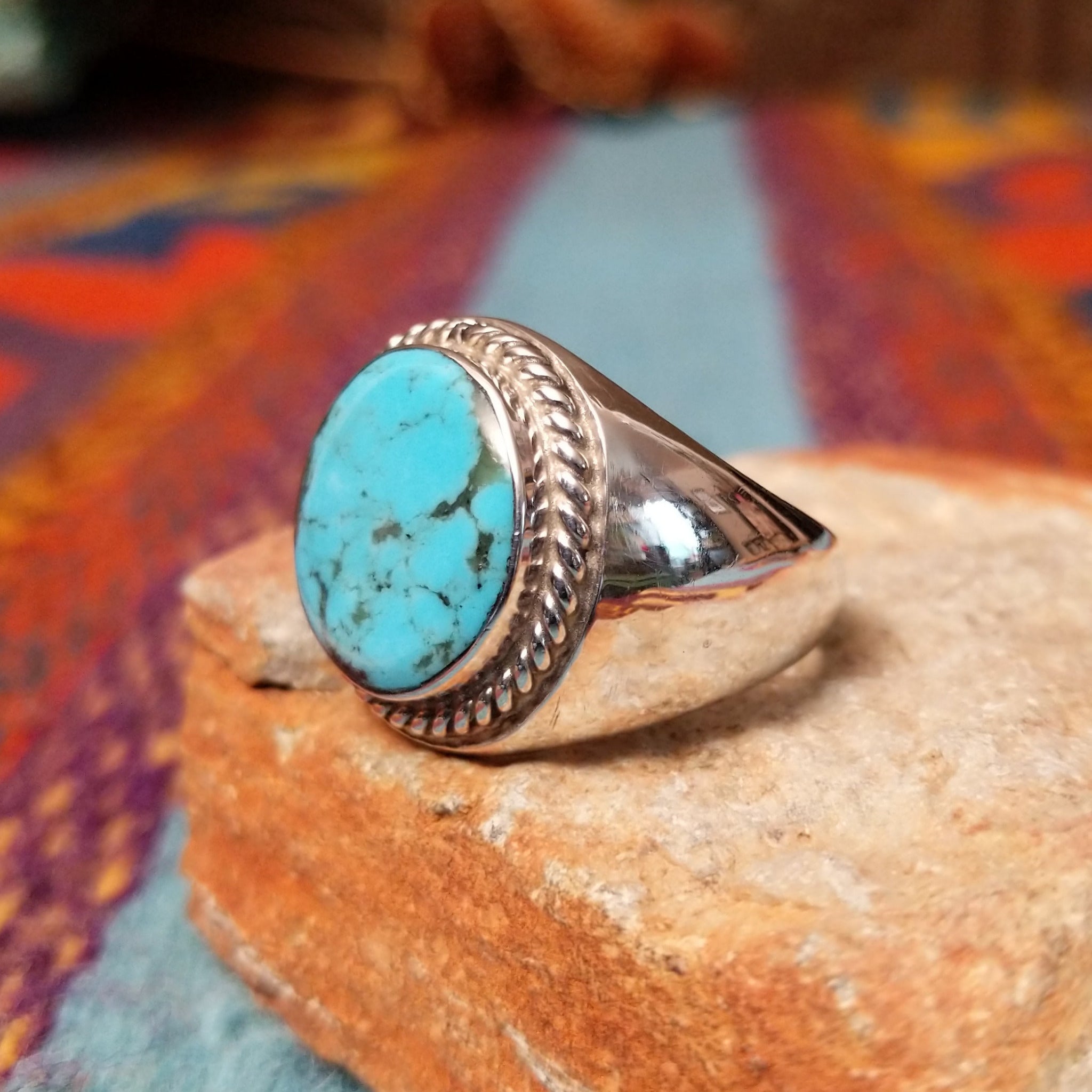 Navajo Turquoise Circle Ring by A.Q.J. featuring a large round turquoise stone with natural dark matrix, framed by twisted rope detailing and set in polished Sterling Silver; side view.