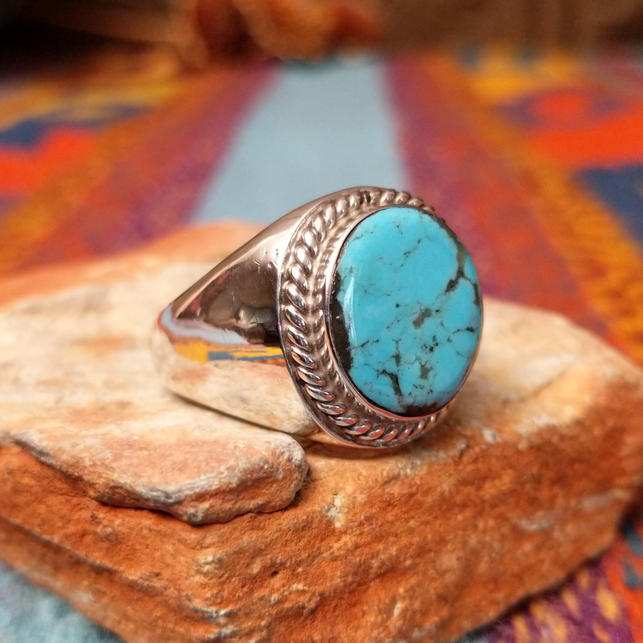 Navajo Turquoise Circle Ring by A.Q.J. featuring a large round turquoise stone with natural dark matrix, framed by twisted rope detailing and set in polished Sterling Silver; side view.