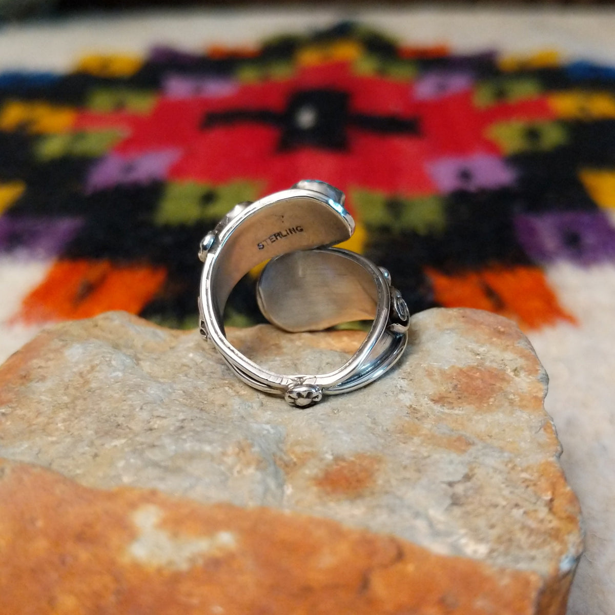 This eye-catching Navajo Turquoise & Coral Feather Ring features turquoise and red coral stones in sawtooth silver bezels with detailed feather, scroll, and silver bead accents; underside view.