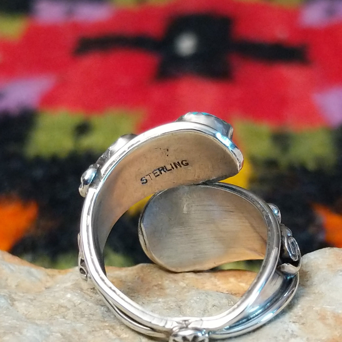 This eye-catching Navajo Turquoise & Coral Feather Ring features turquoise and red coral stones in sawtooth silver bezels with detailed feather, scroll, and silver bead accents; Sterling Silver stamp.