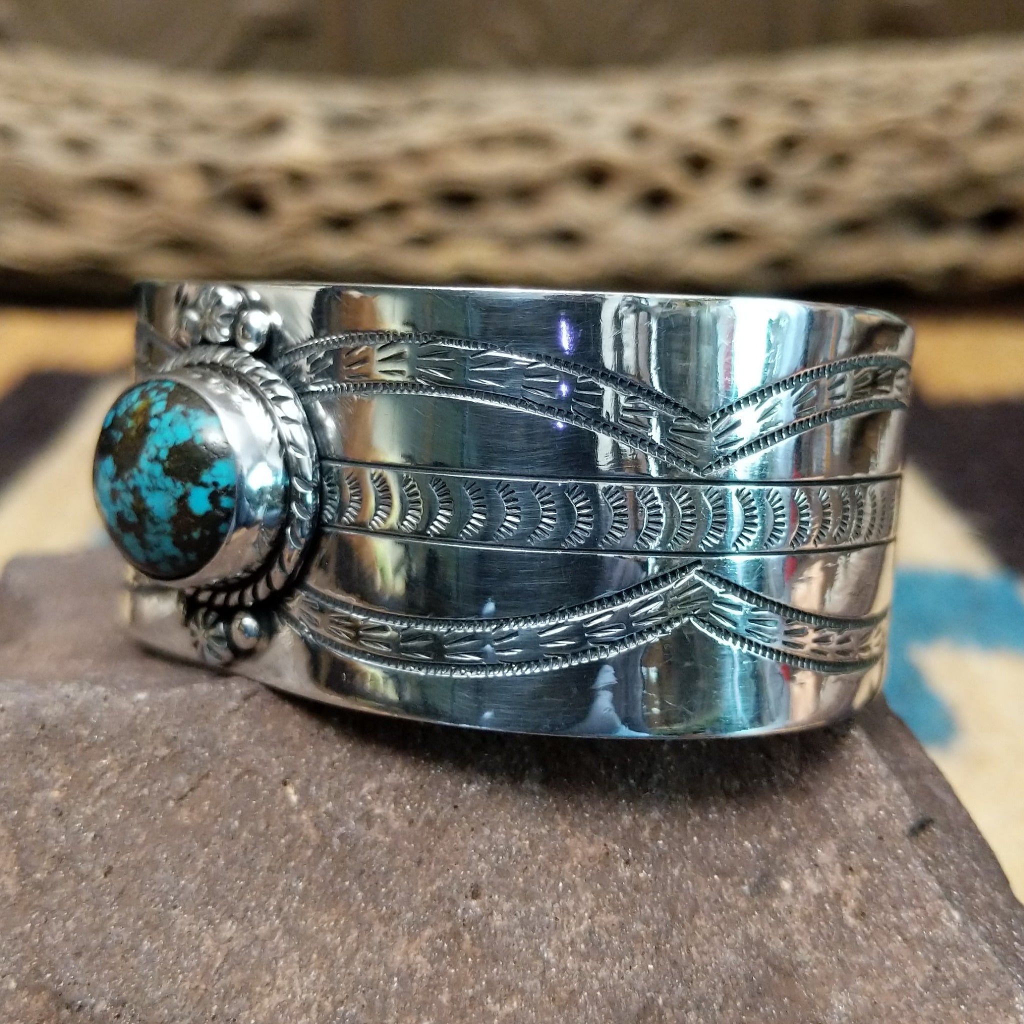 Navajo turquoise cuff by L.T.C., featuring an oval blue turquoise stone with natural black matrix set in a handcrafted sterling silver cuff with hand-stamped details, decorative silver accents, and a twisted rope bezel; side view.