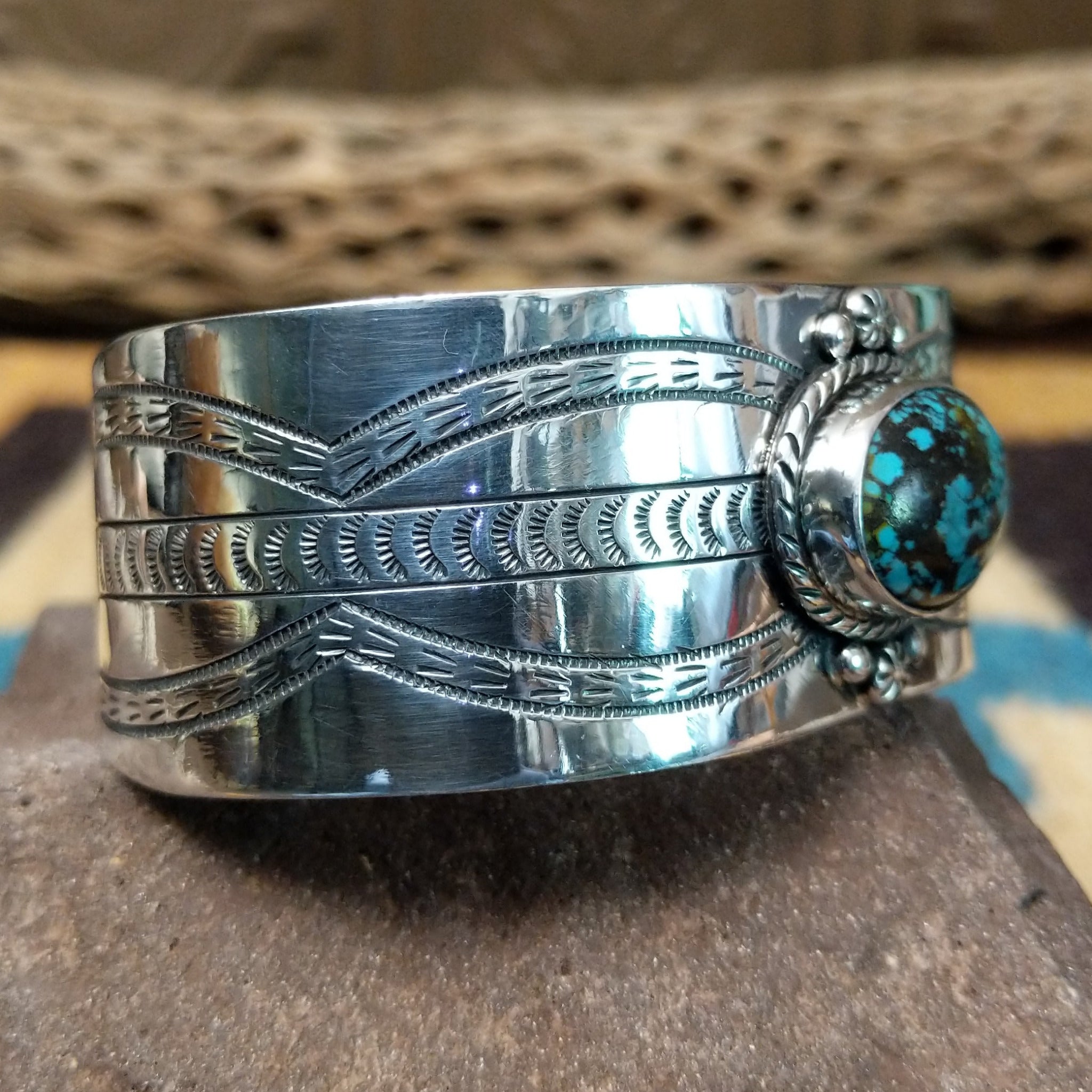 Navajo turquoise cuff by L.T.C., featuring an oval blue turquoise stone with natural black matrix set in a handcrafted sterling silver cuff with hand-stamped details, decorative silver accents, and a twisted rope bezel; side view.