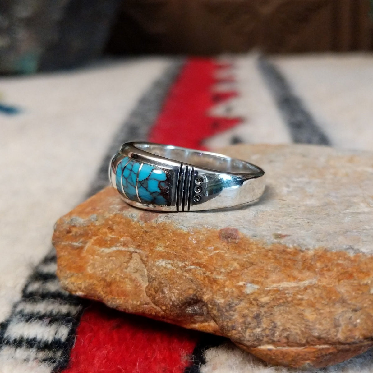Navajo turquoise inlay ring featuring bright blue turquoise with dark matrix, segmented by polished silver channels across a wide silver band; side view.