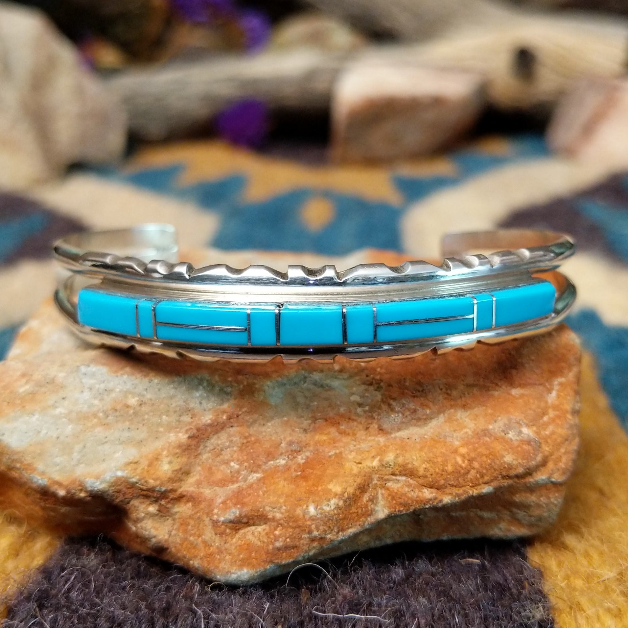 Handcrafted sterling silver Navajo cuff by E. featuring a vibrant row of turquoise channel inlay with a polished silver frame and scalloped edge detailing.
