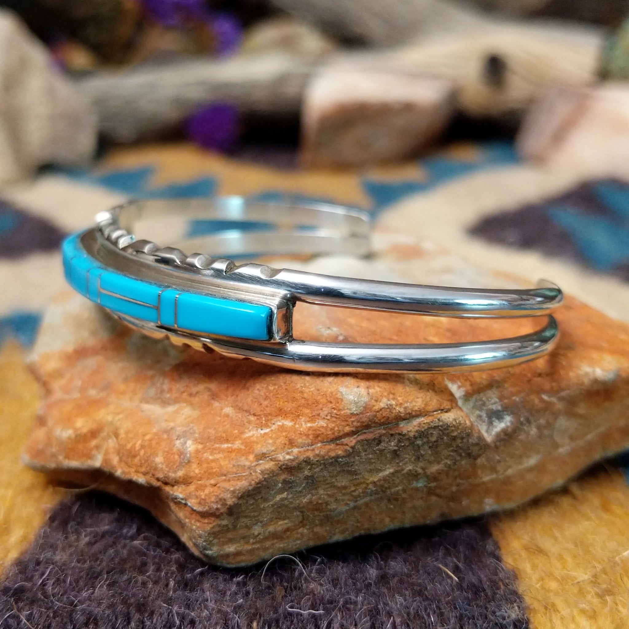 Handcrafted sterling silver Navajo cuff by E. featuring a vibrant row of turquoise channel inlay with a polished silver frame and scalloped edge detailing; side view.