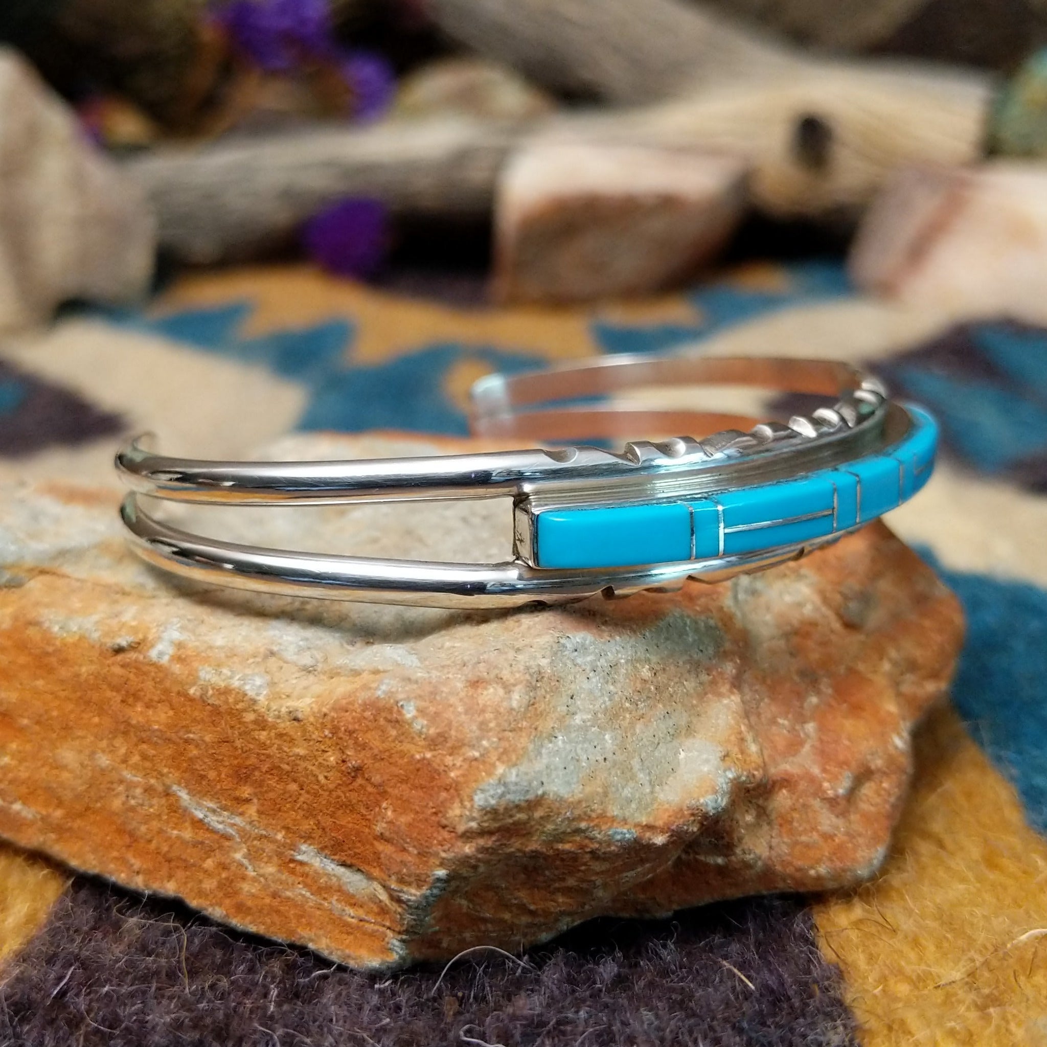 Handcrafted sterling silver Navajo cuff by E. featuring a vibrant row of turquoise channel inlay with a polished silver frame and scalloped edge detailing; side view.