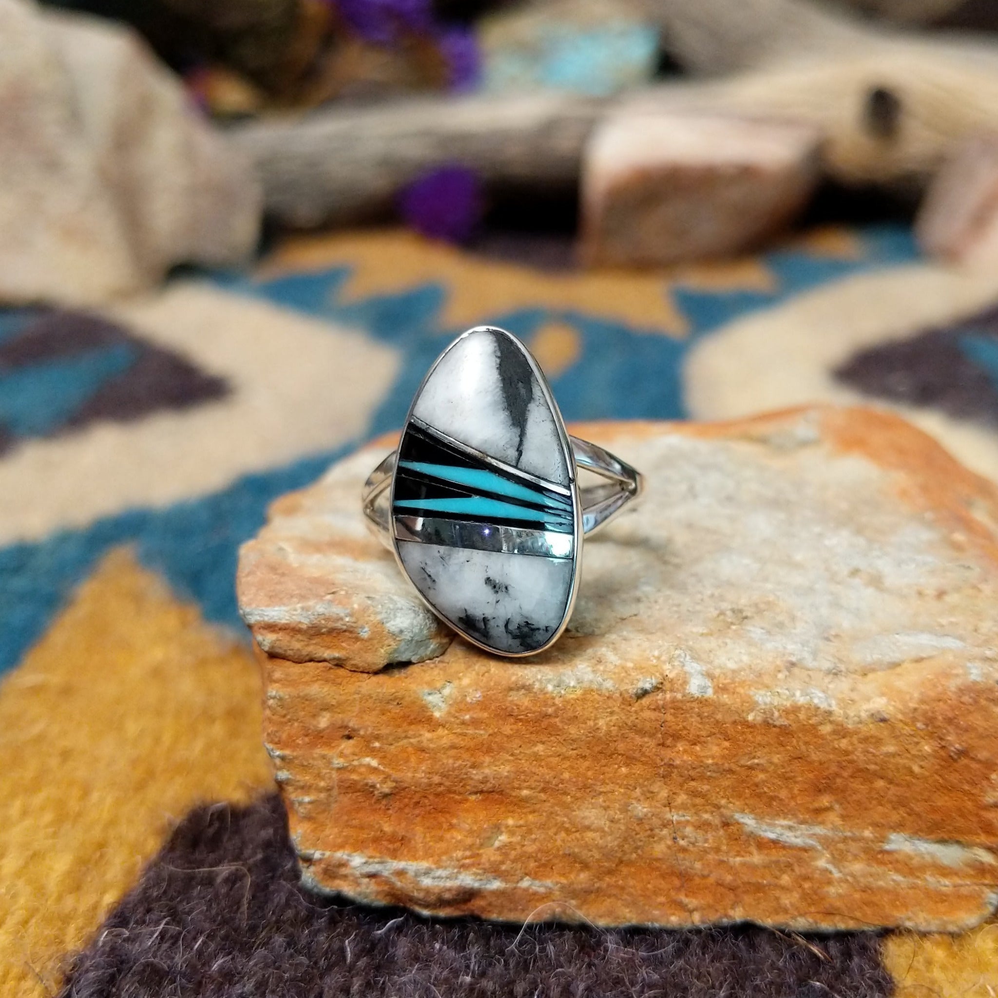 Handcrafted Navajo sterling silver ring featuring an elongated oval White Buffalo inlay with black onyx, turquoise, and sterling silver geometric accents in a polished bezel setting.