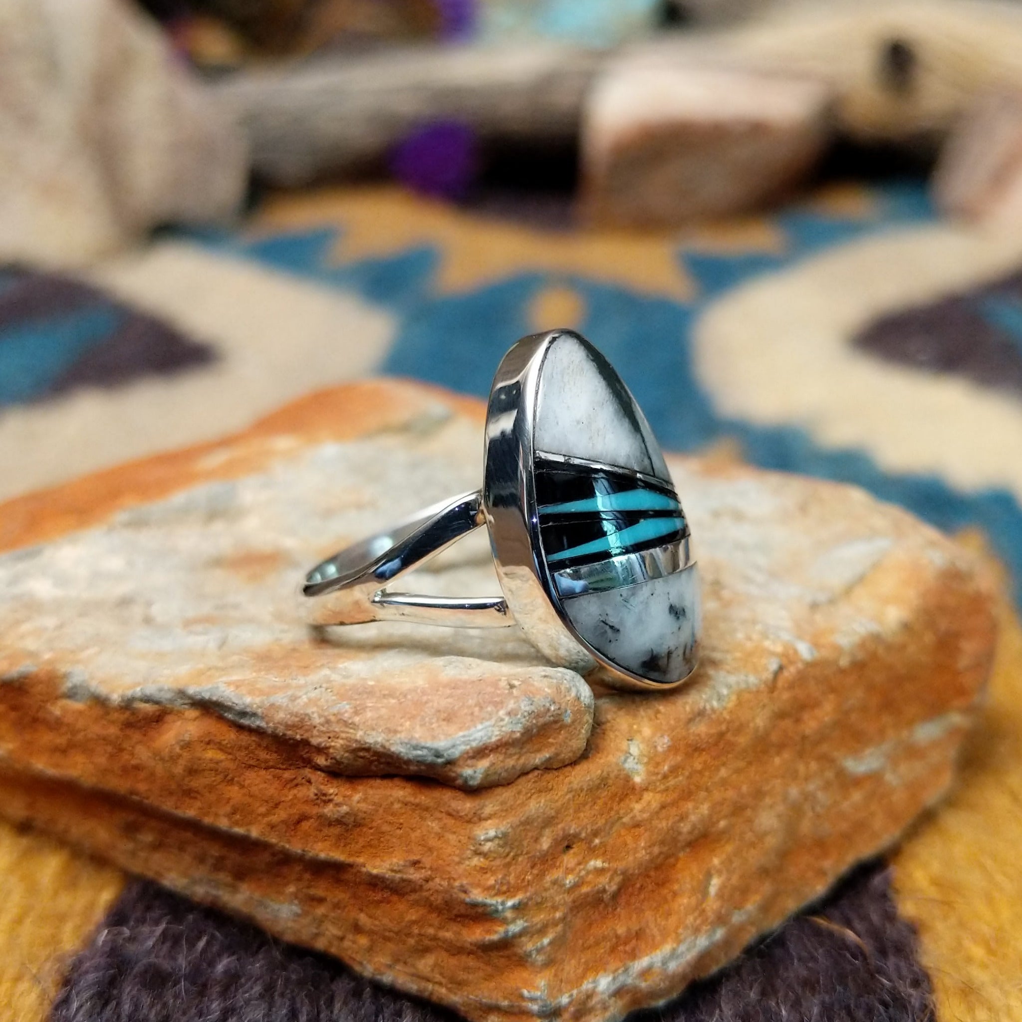 Handcrafted Navajo sterling silver ring featuring an elongated oval White Buffalo inlay with black onyx, turquoise, and sterling silver geometric accents in a polished bezel setting; side view.