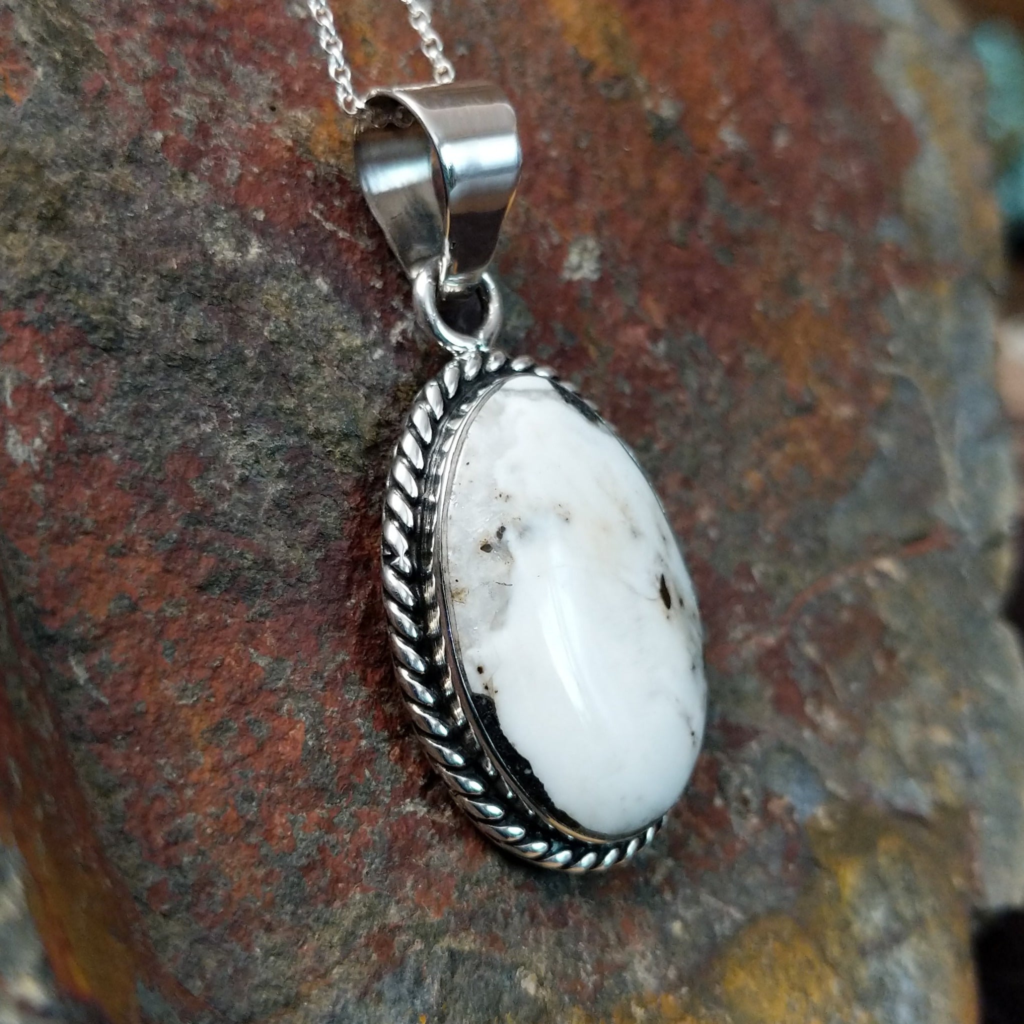 Handcrafted sterling silver Navajo White Buffalo portrait pendant by K., featuring a natural White Buffalo gemstone in a twisted rope bezel setting; side view.