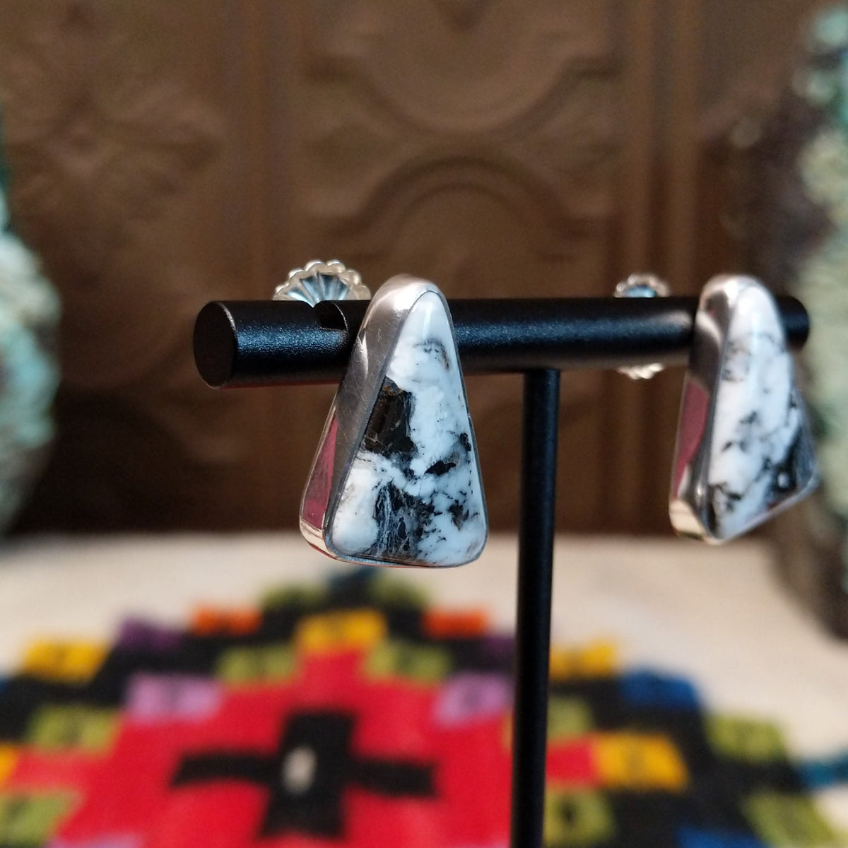 Navajo White Buffalo Triangle Earrings by L.P. featuring polished triangular white stones with natural black matrix patterns set in smooth silver bezels; side view.