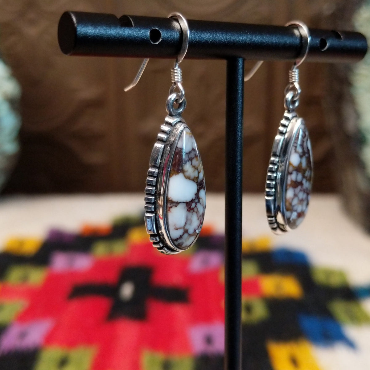Navajo Wild Horse Teardrop Earrings by B.A. featuring polished white and reddish-brown matrix stones in detailed silver settings with French ear wires; side view.