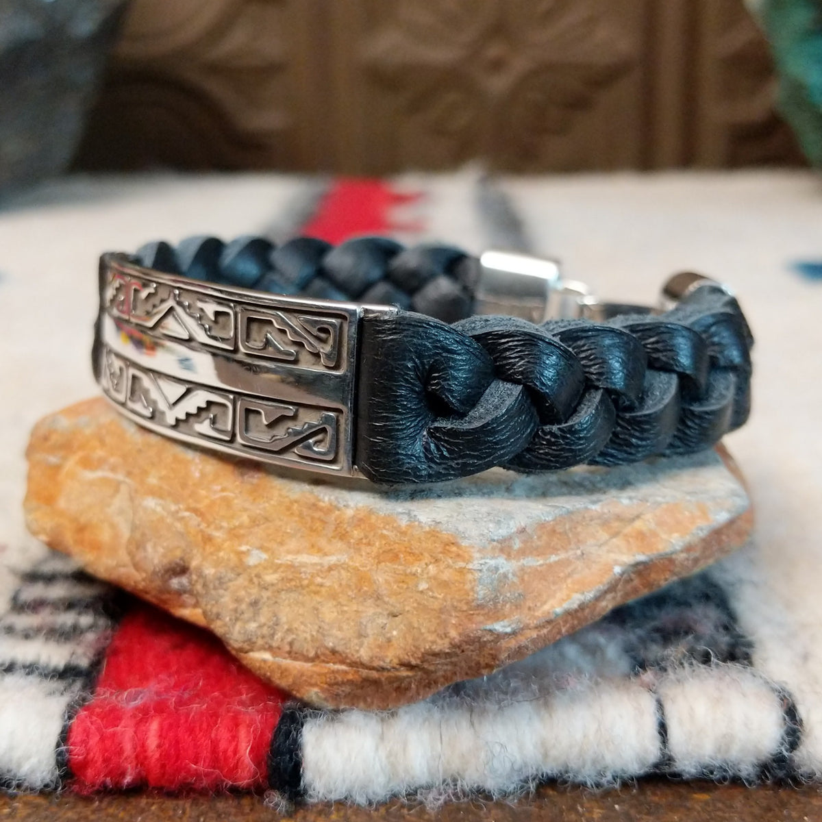 Navajo bracelet with braided black leather and a rectangular polished silver centerpiece featuring repeating stepped geometric patterns and central triangular designs; side view.